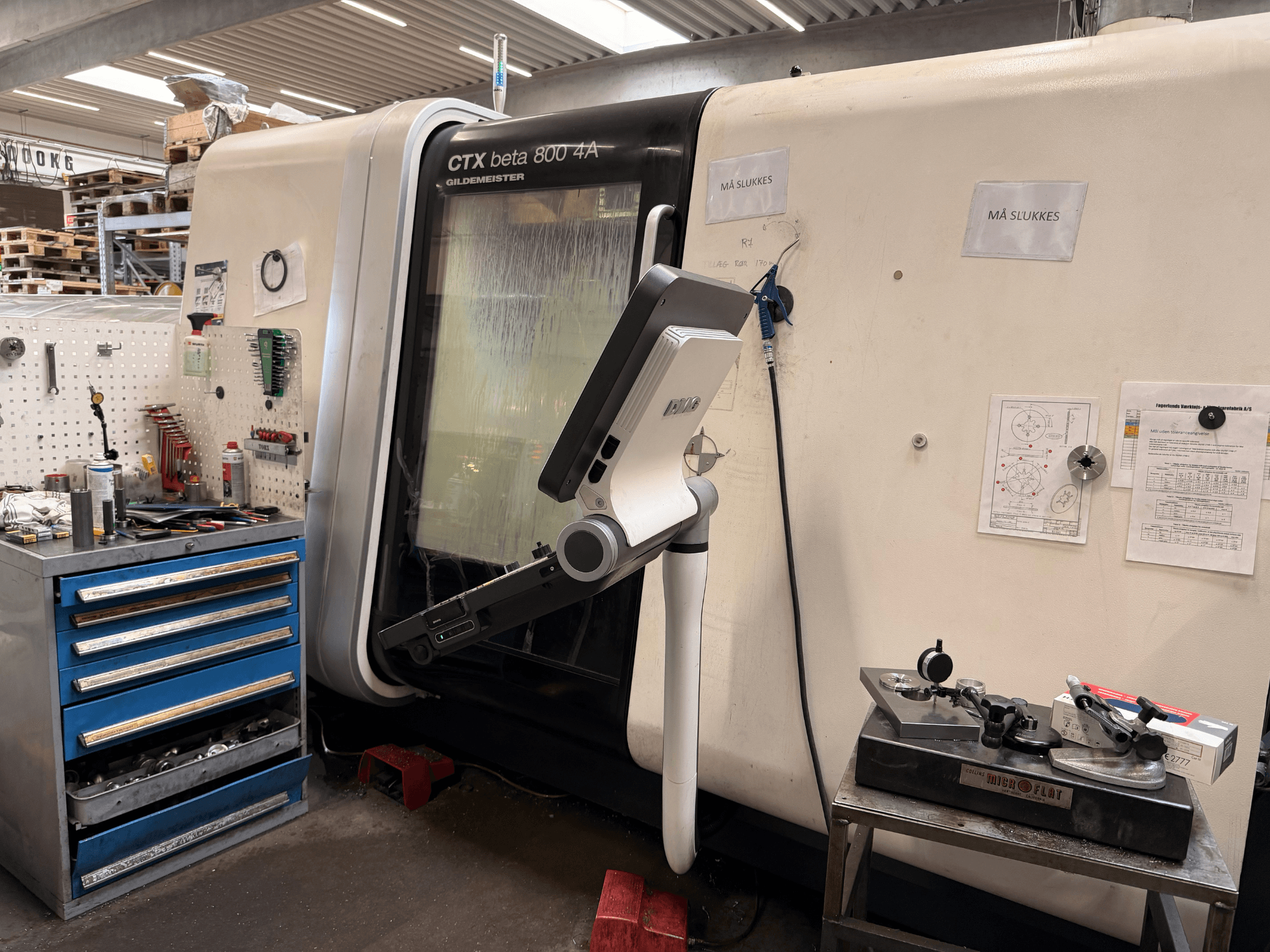DMG MORI CTX Beta 800 4a vertical turning machine in a workshop, featuring a control arm and technical documents nearby.