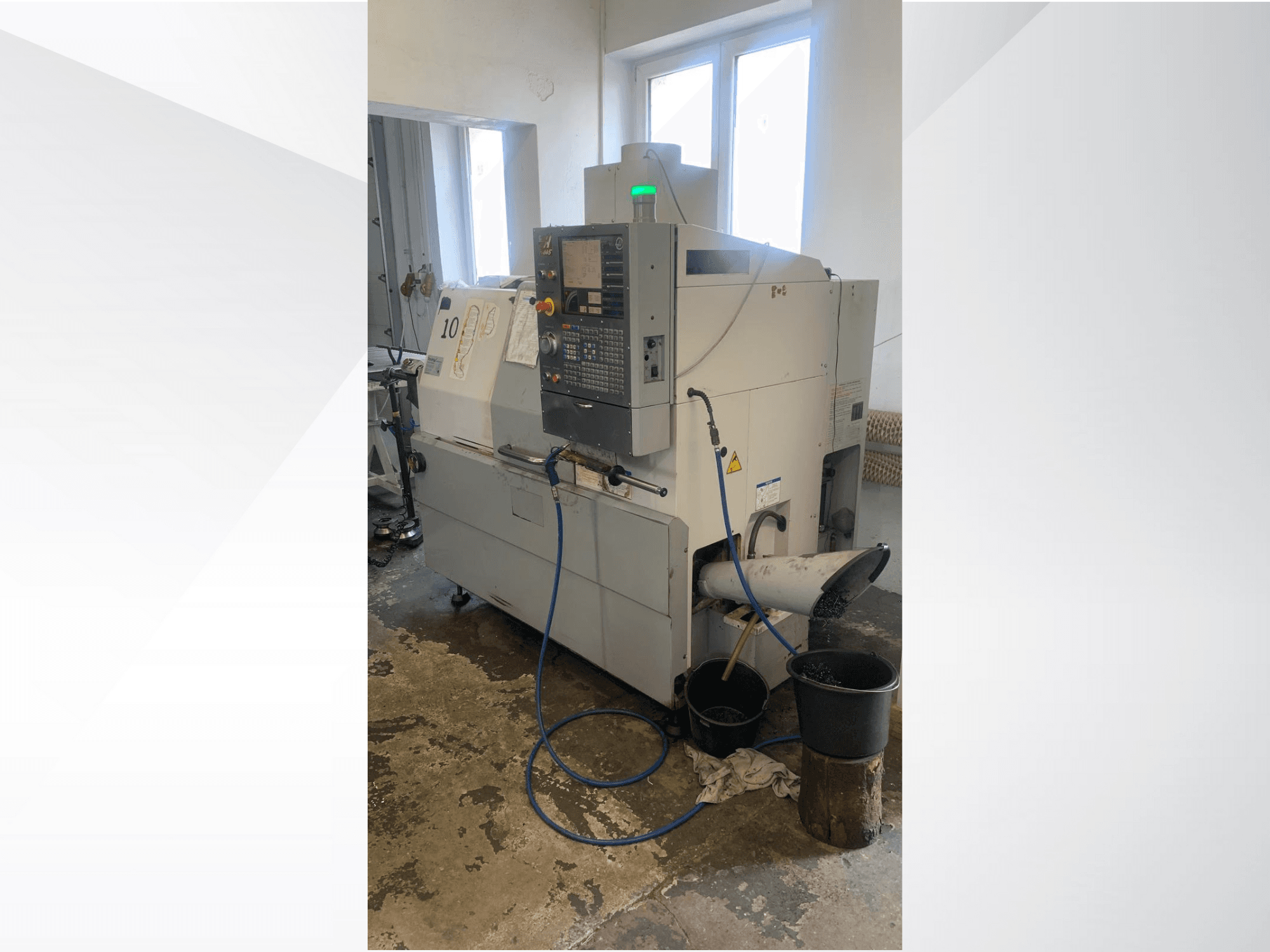 Haas CNC machine model with control panel, side view, featuring coolant line, waste chute, and storage containers below.