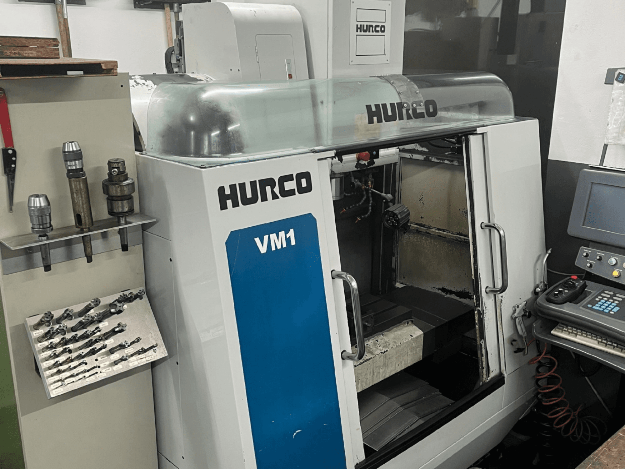 Hurco VM1 vertical machining center front view, featuring a transparent cover, control panel, and mounted tools.