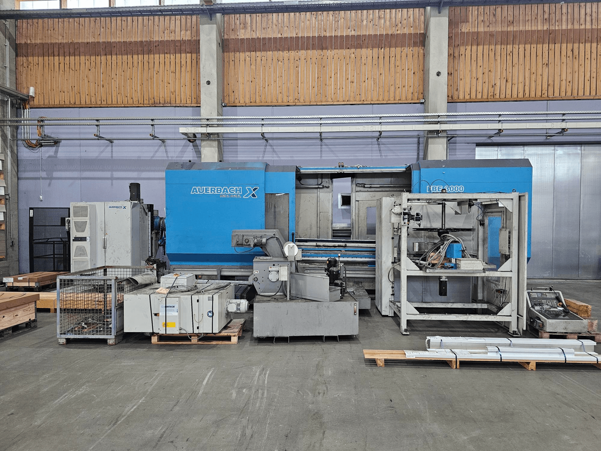 Auerbach X LBF-3000 machine in a factory setting, side view, featuring grey and blue components with visible control panel.