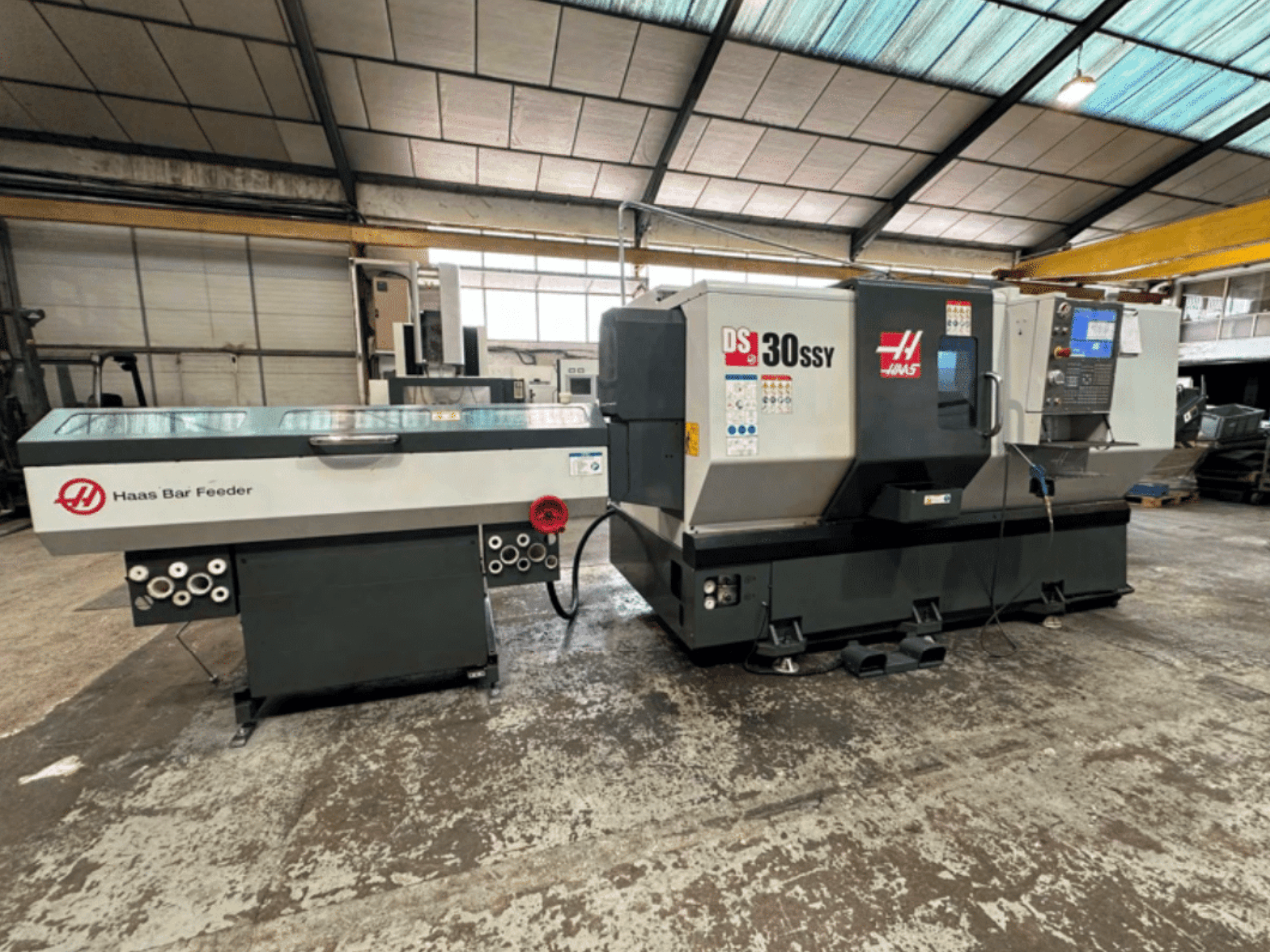 Haas DS-30SSY CNC lathe with Haas Bar Feeder, side view showcasing control panel and feed mechanism in a workshop setting.