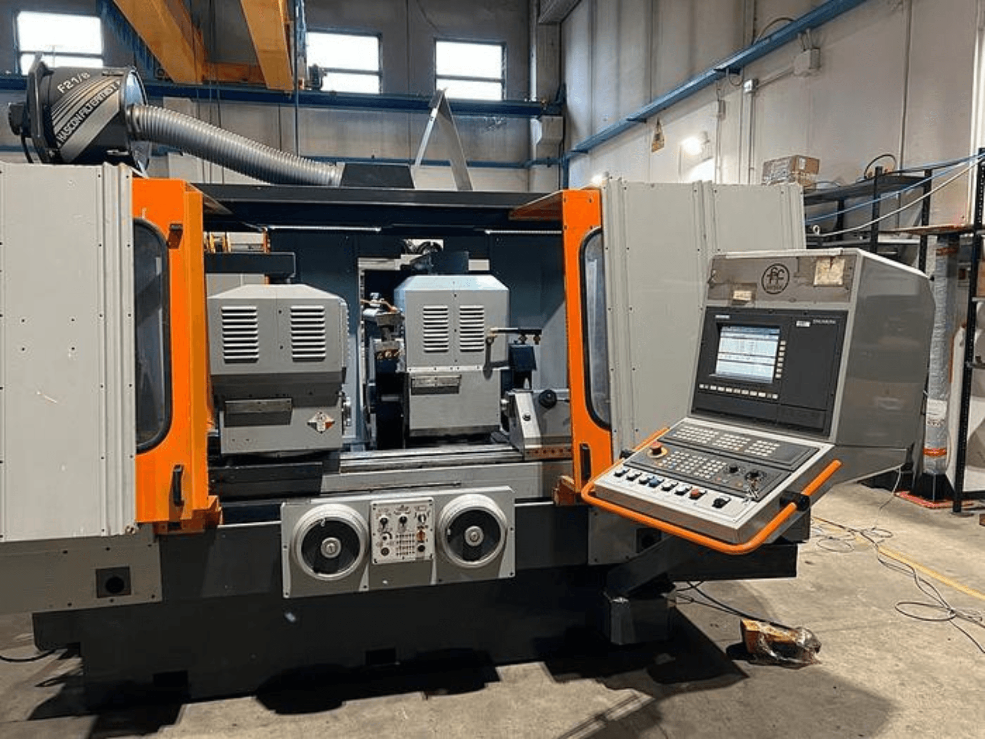 Front view of a CNC machine with dual spindles, control panel, and orange accents. Features ventilation duct and operational controls.