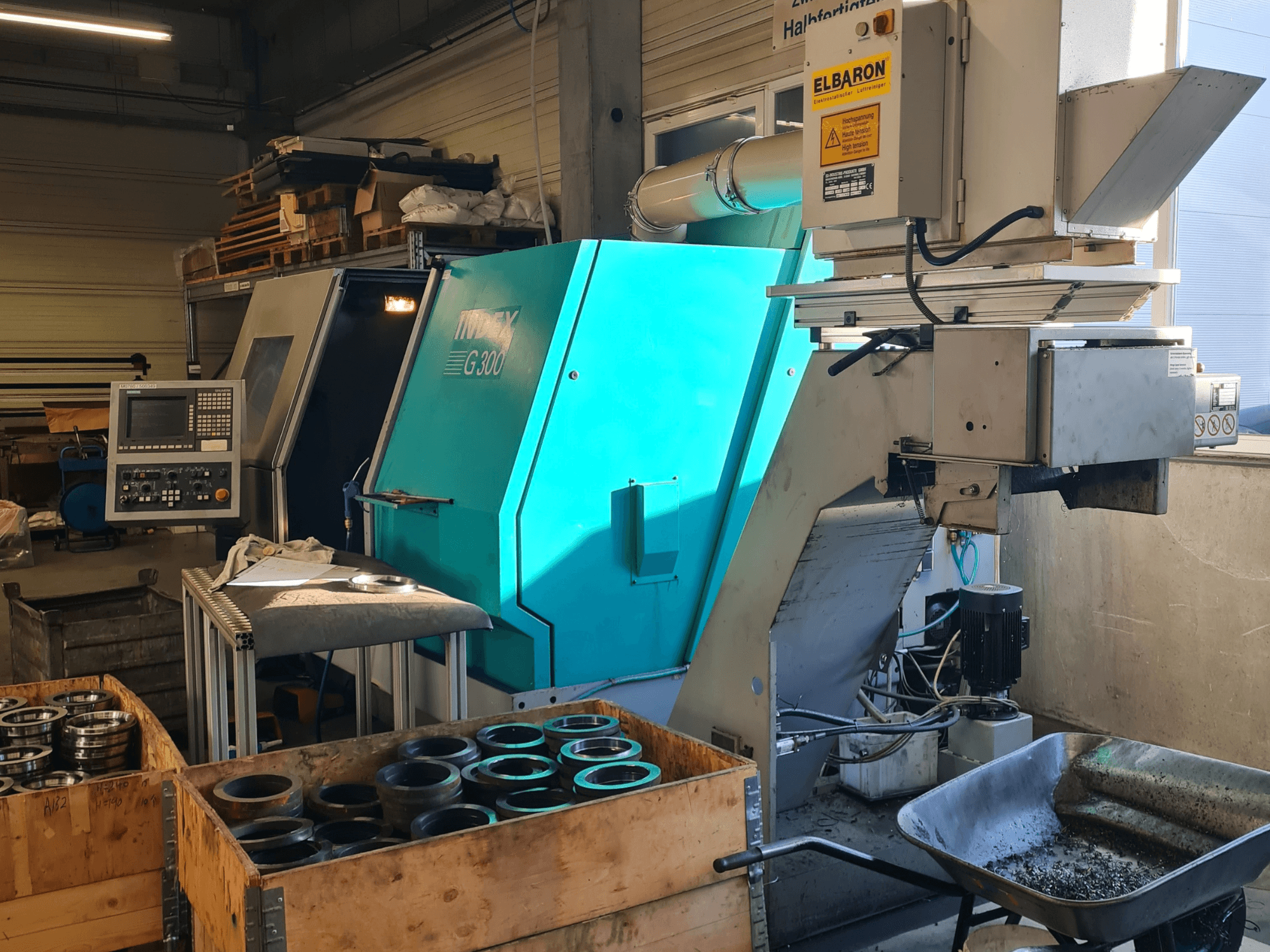 Front view of the Index G300 RatioLine horizontal turning machine with control panel, surrounded by parts and a conveyor.