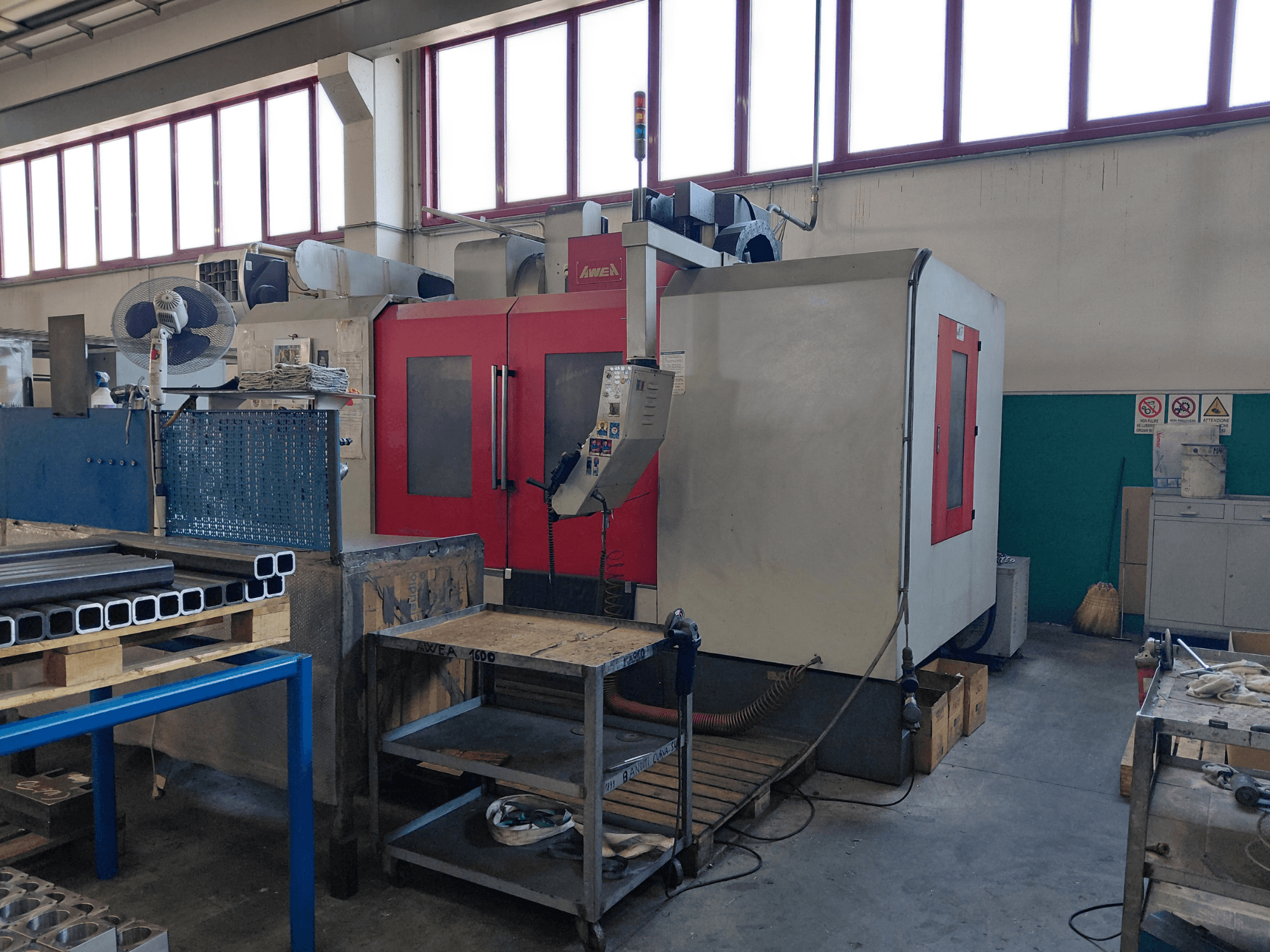 AWEA BM-1600 vertical machining centre, front view, with red and gray body, nearby workbench and tools visible.