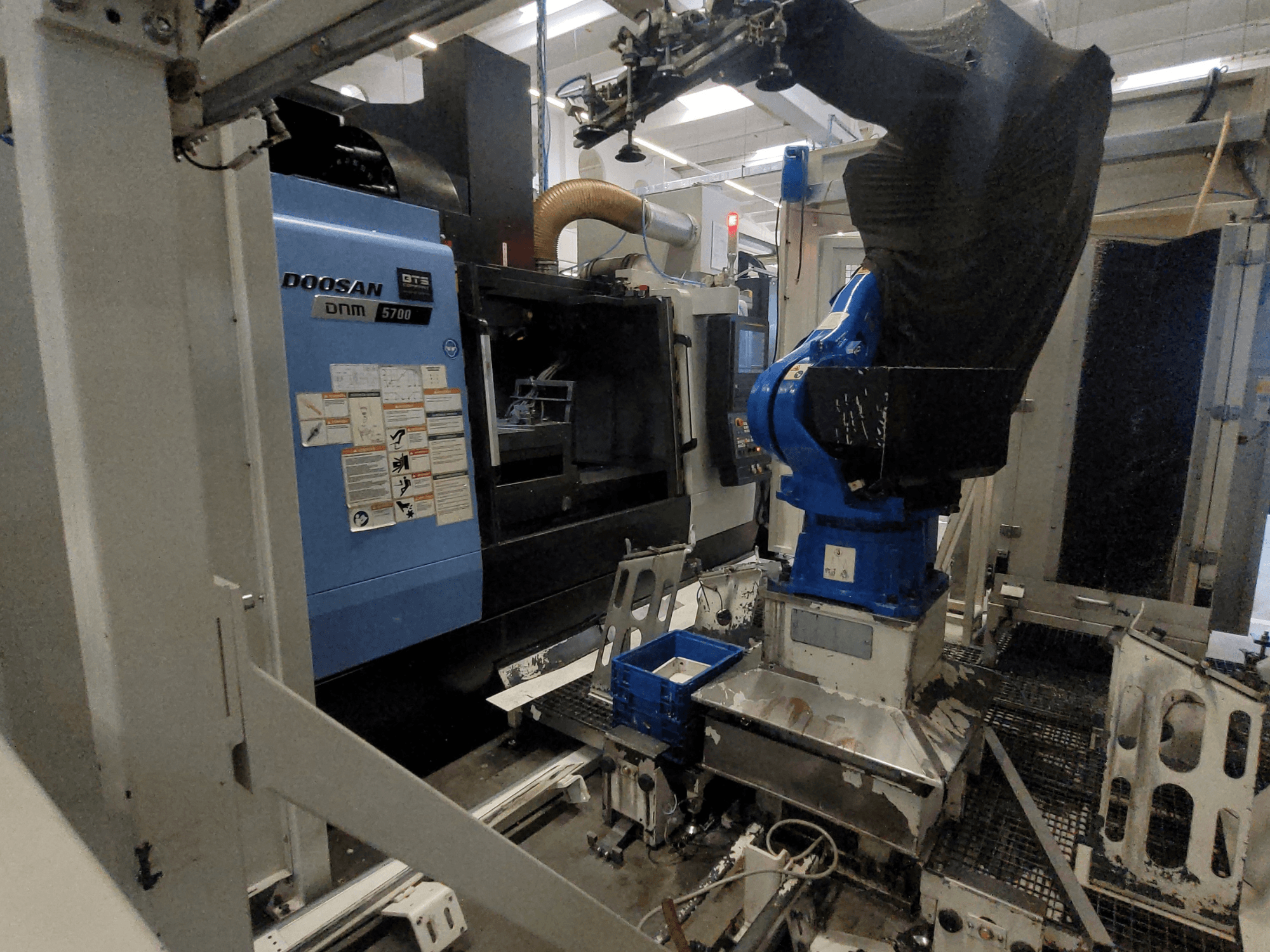 DOOSAN DNM 5700 vertical machining center in a factory setting, showcasing its front view and robotic arm integration.