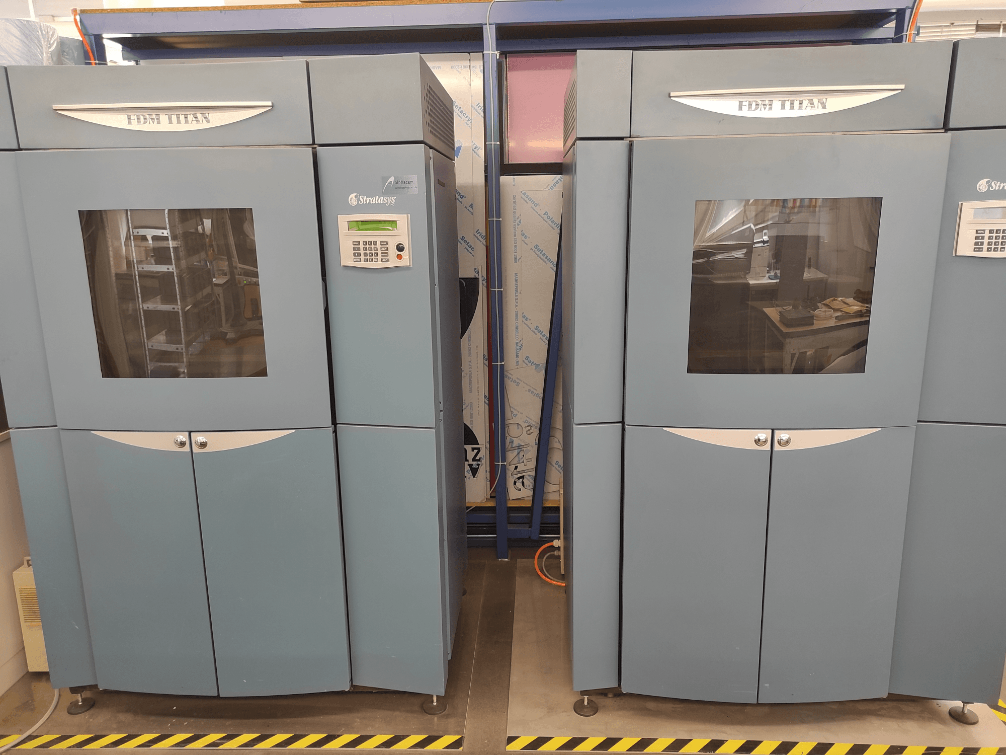 FDM TitanTI 3D printer by Stratasys, front view, featuring dual doors and control panel, set in an industrial environment.