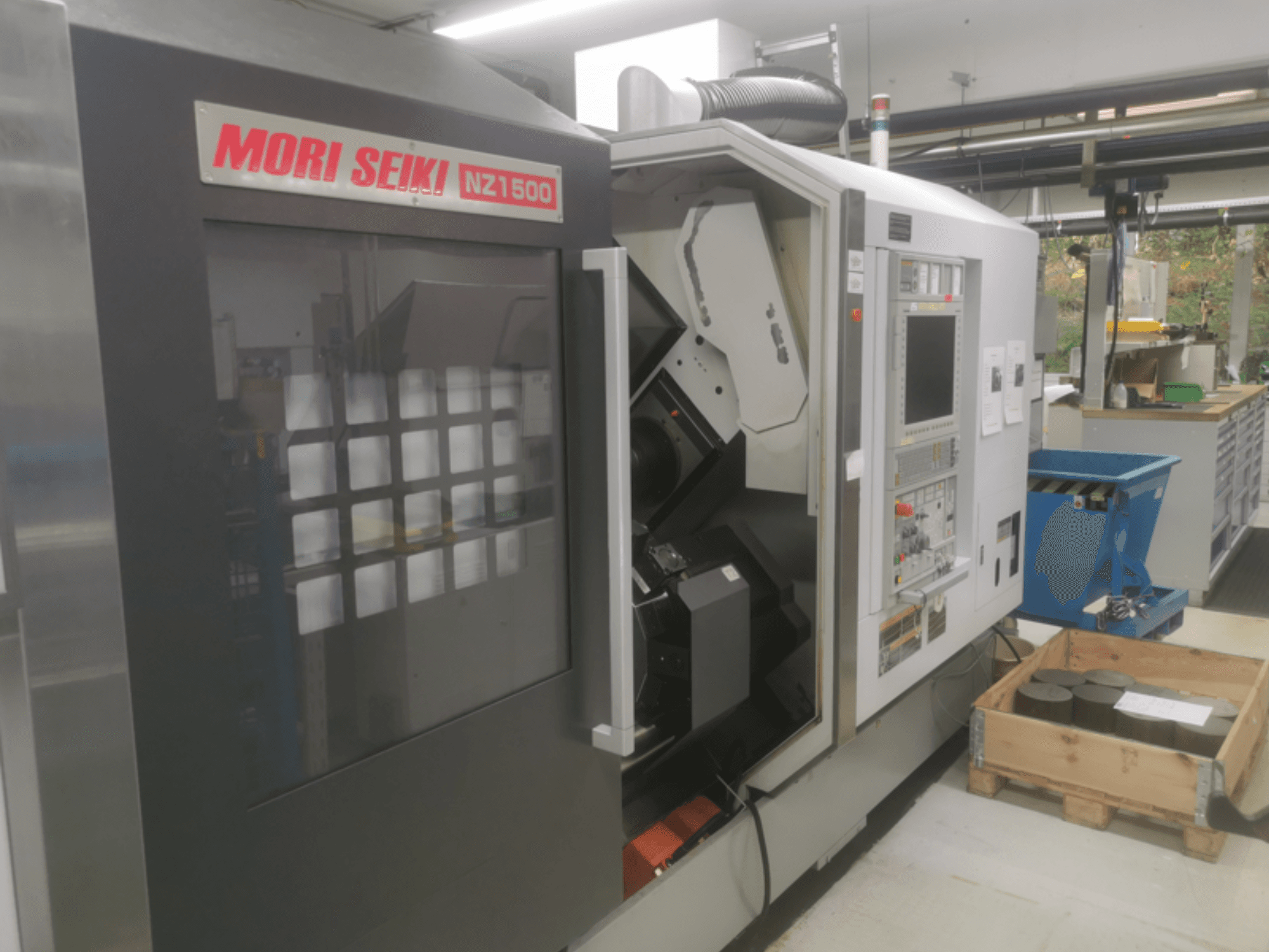 MORI SEIKI NZ1500 CNC machine at a slight angle, showing control panel and workspace with metal workpieces on a wooden pallet.