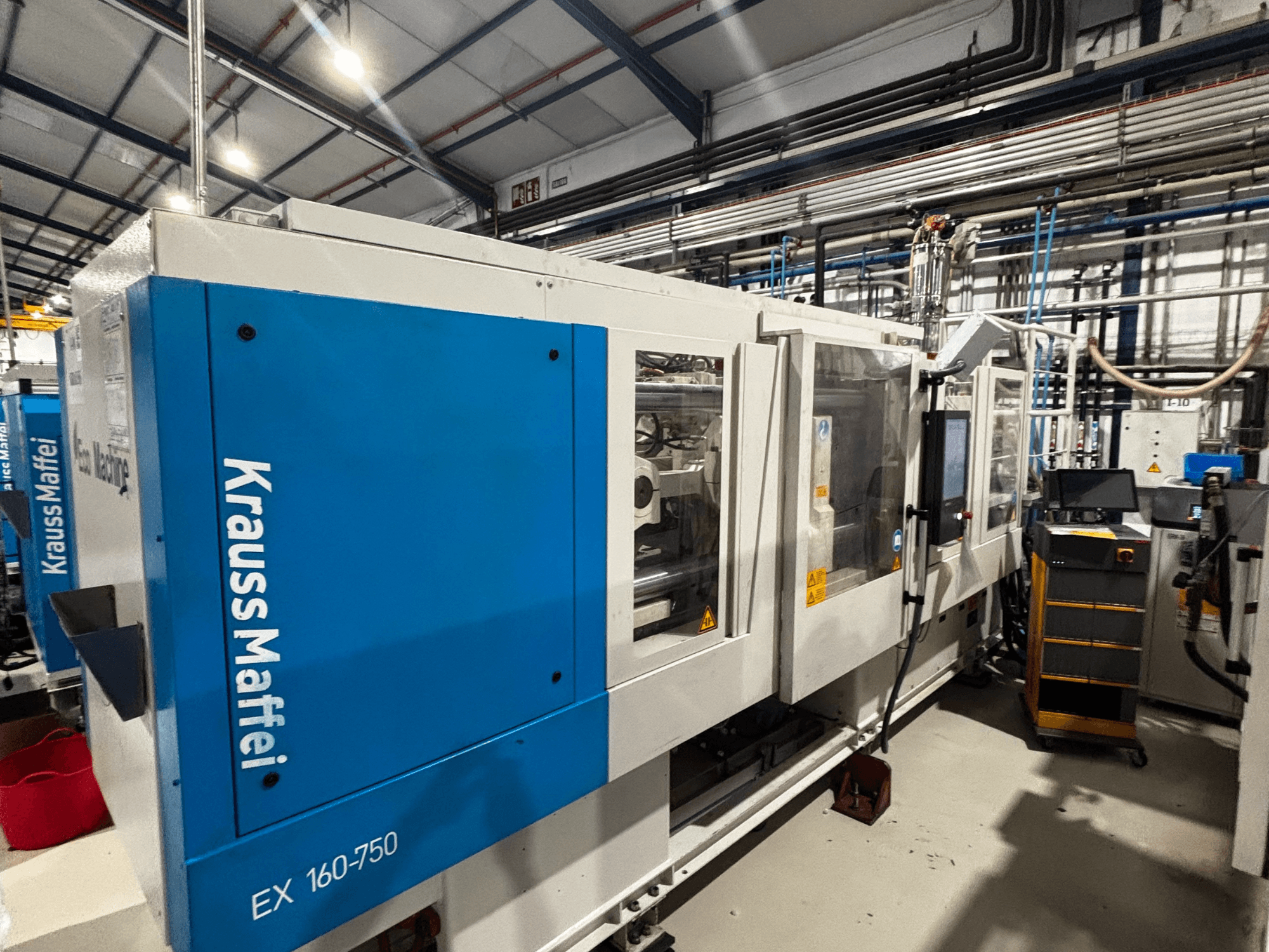 KraussMaffei EX 160-750 injection molding machine in a factory, side view with control panel and automated system visible.