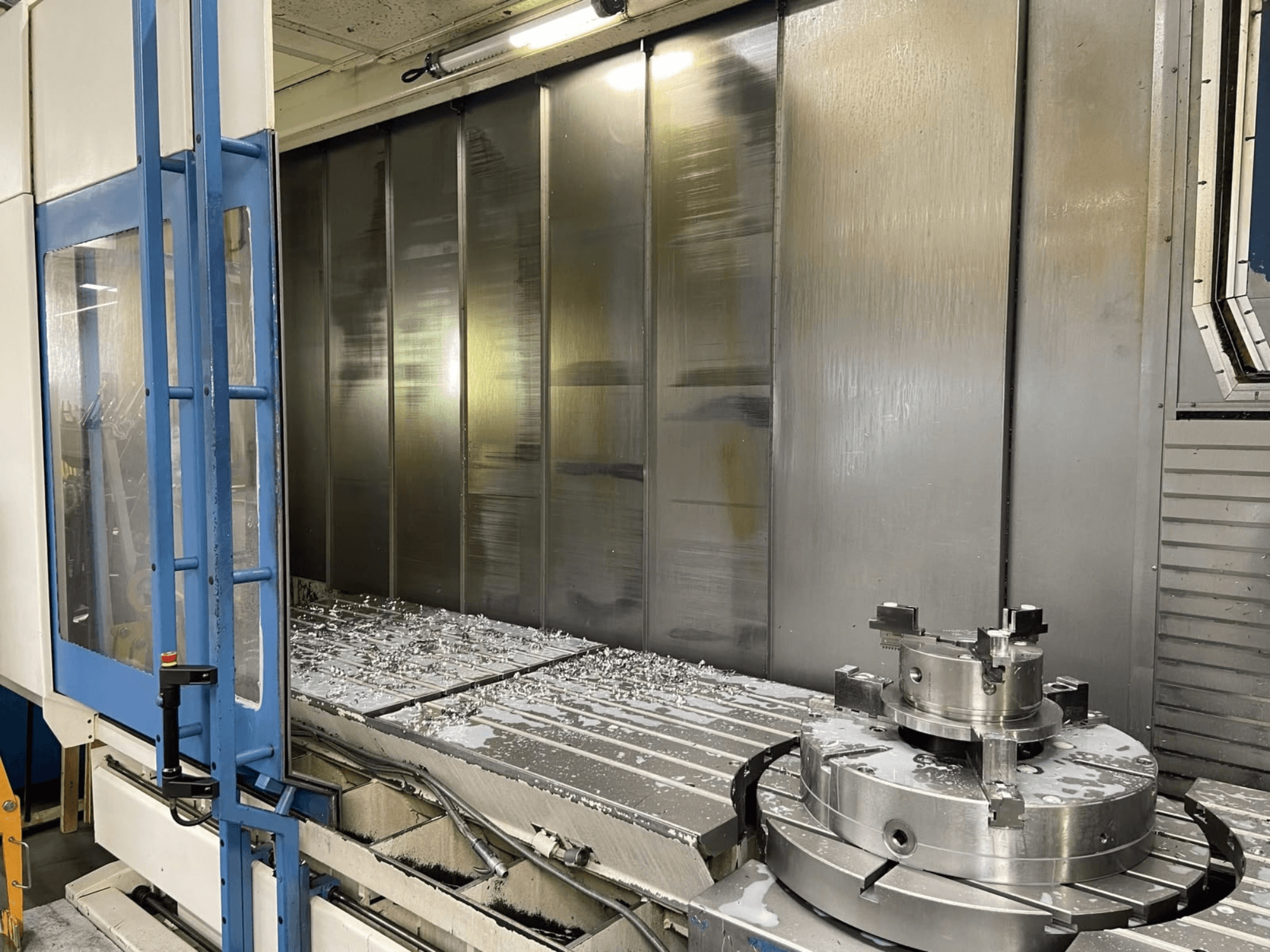 AXA VHC-3-3000-M/E vertical machining center, front view, showing milled metal shavings on the worktable and cutting tools.