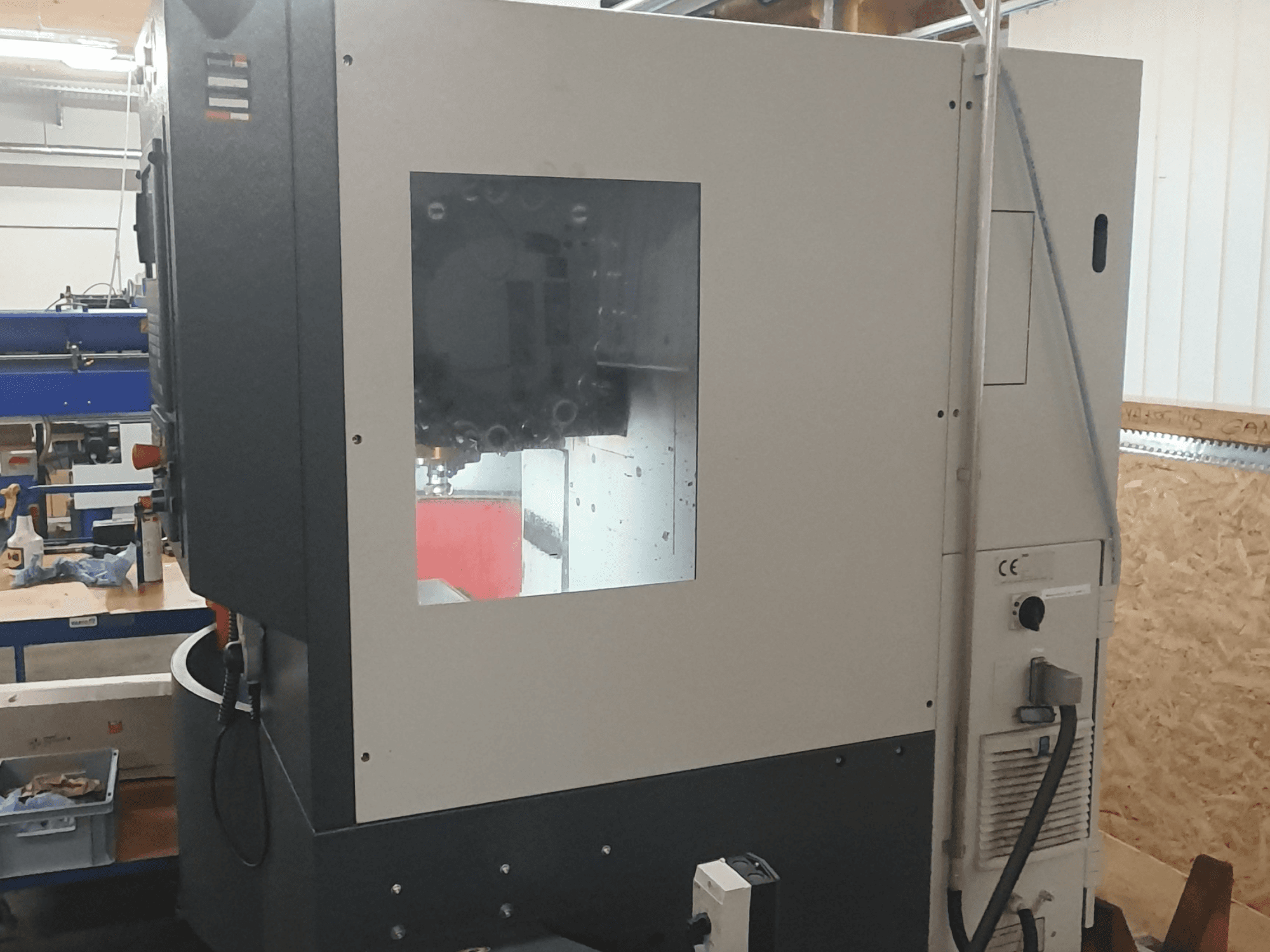 Side view of a metalworking machine with visible control panel, large viewing window, and intricate inner components.