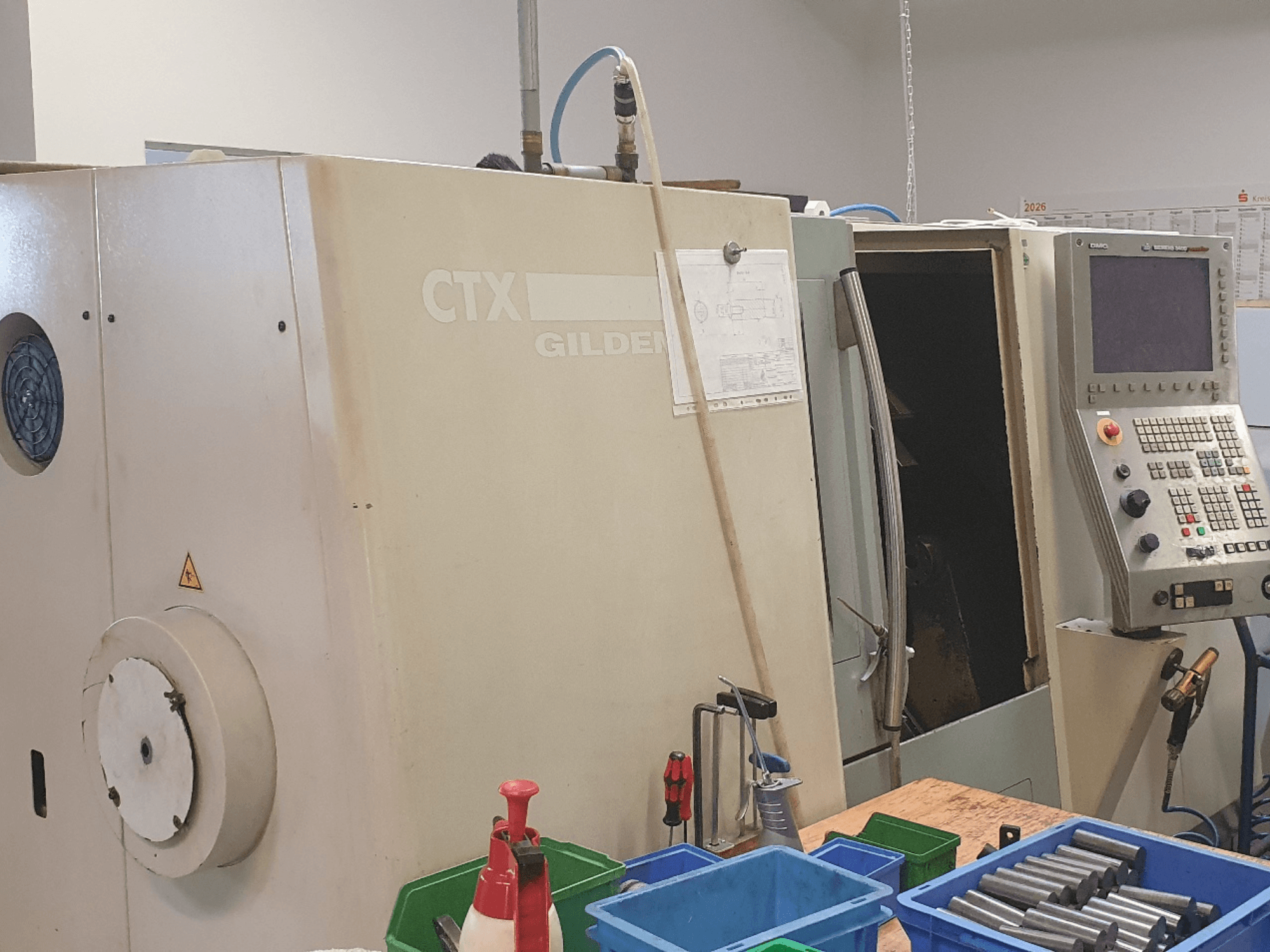 Front view of DMG GILDEMEISTER CTX 310 horizontal turning machine, control panel visible, tools and containers in foreground.