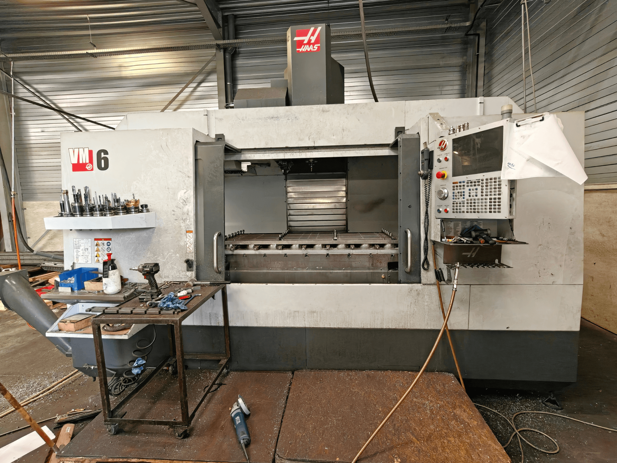 Haas VM-6 vertical machining center, front view, with tool storage, control panel, and work area debris visible.
