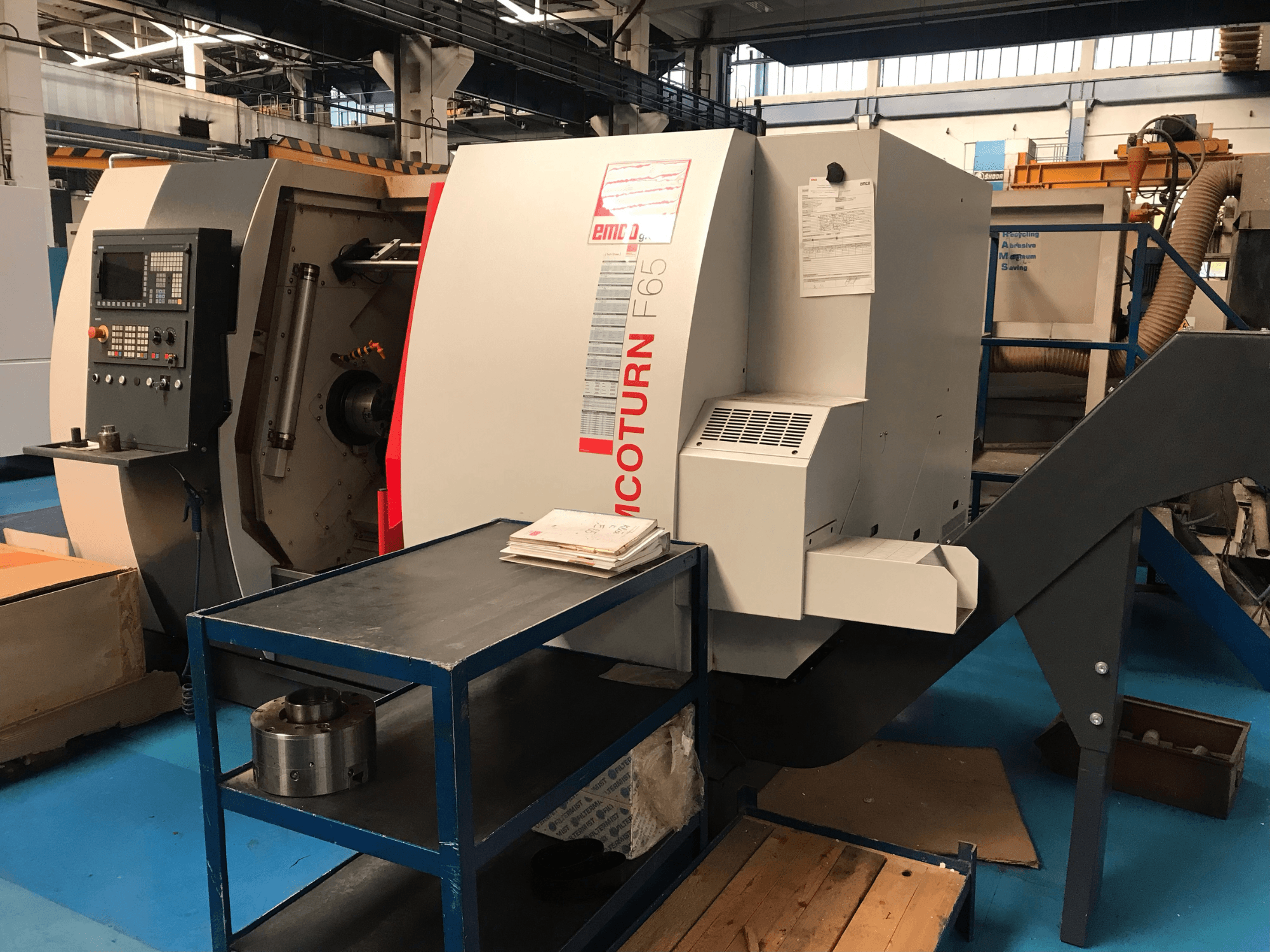 EMCO Emcoturn 65 horizontal turning machine from a side view, showcasing controls and workspace with metal parts nearby.