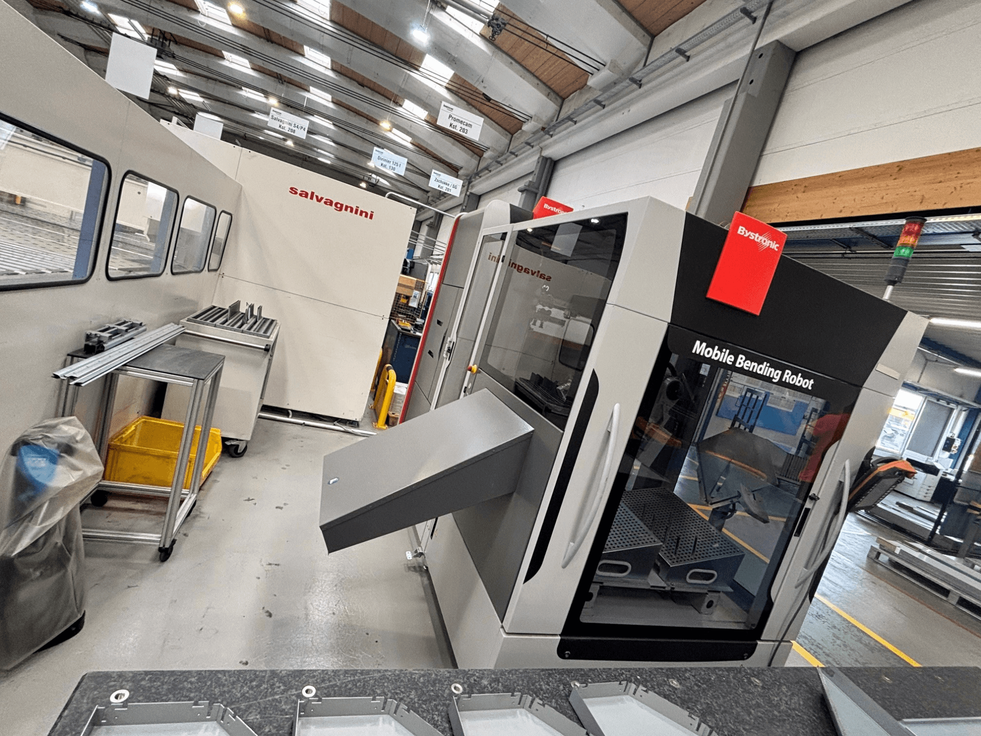Bystronic Xpert 40/1030 press brake, front view showing mobile bending robot and work area with metal parts on a table.