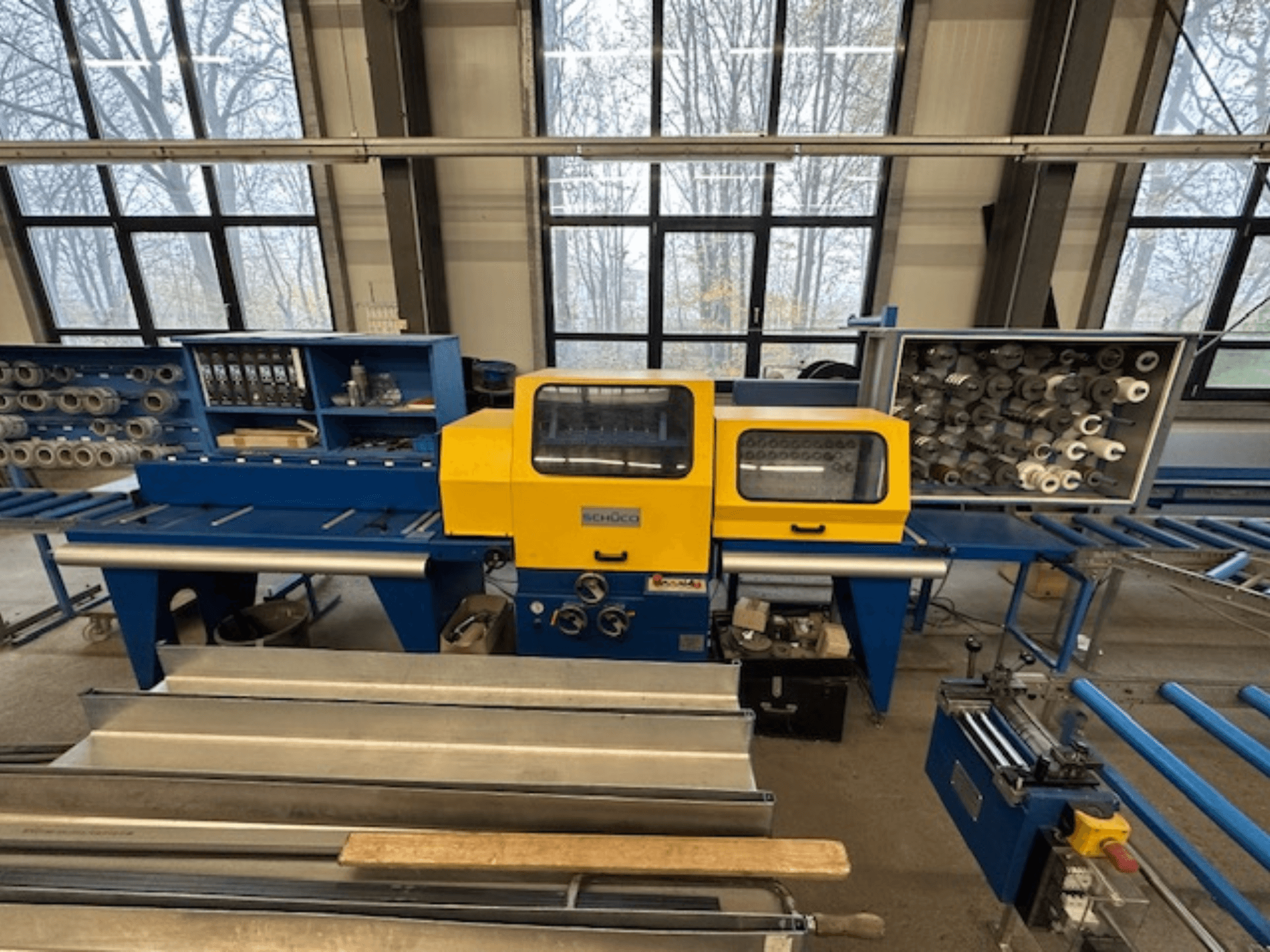 Front view of SCHÜCO ISOMAT 4 machine tool, featuring a yellow control panel, multiple rolls, and a storage compartment.