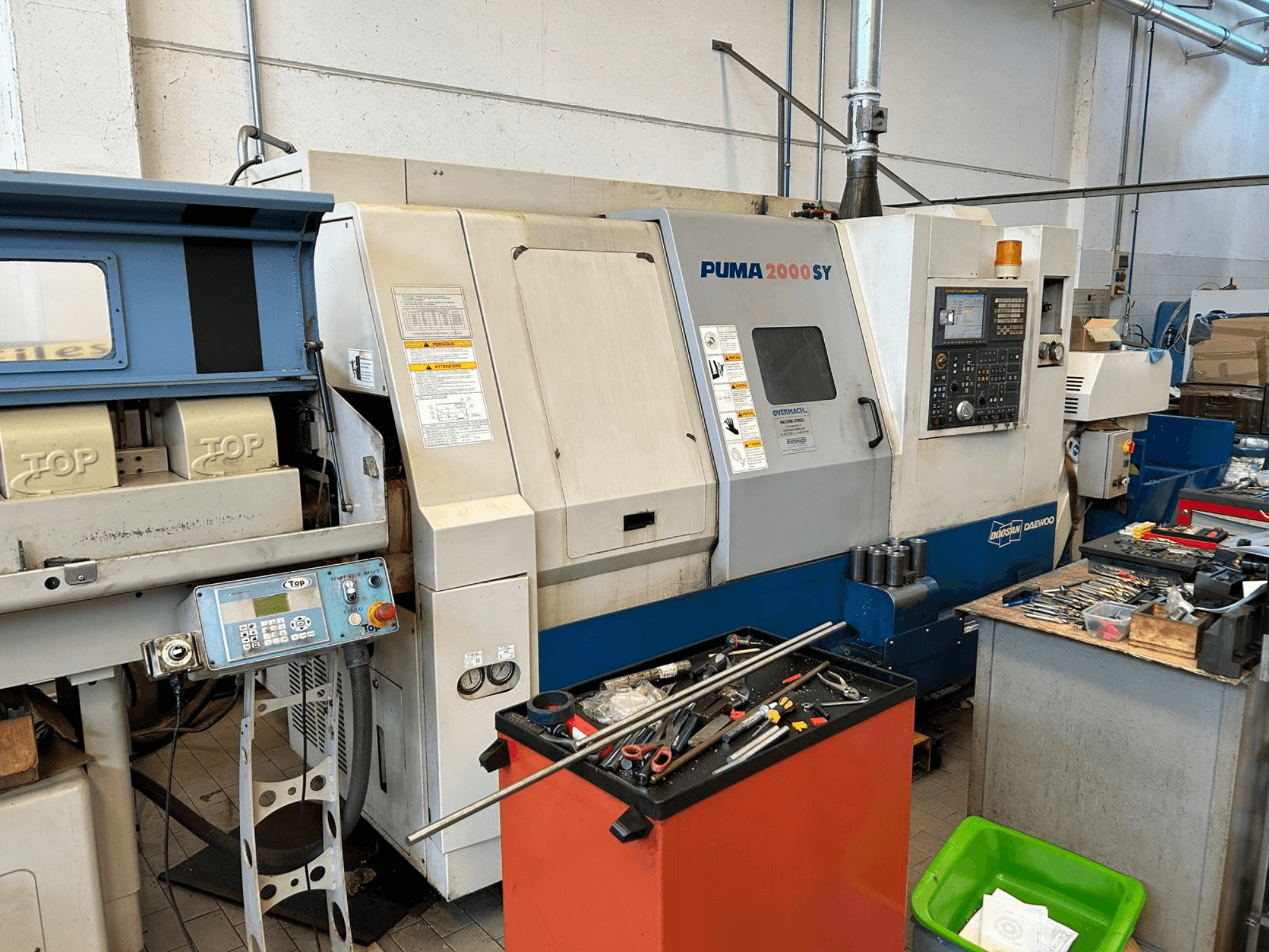 DOOSAN PUMA 2000SY horizontal turning machine in a workshop, side view showcasing control panel and tools nearby.