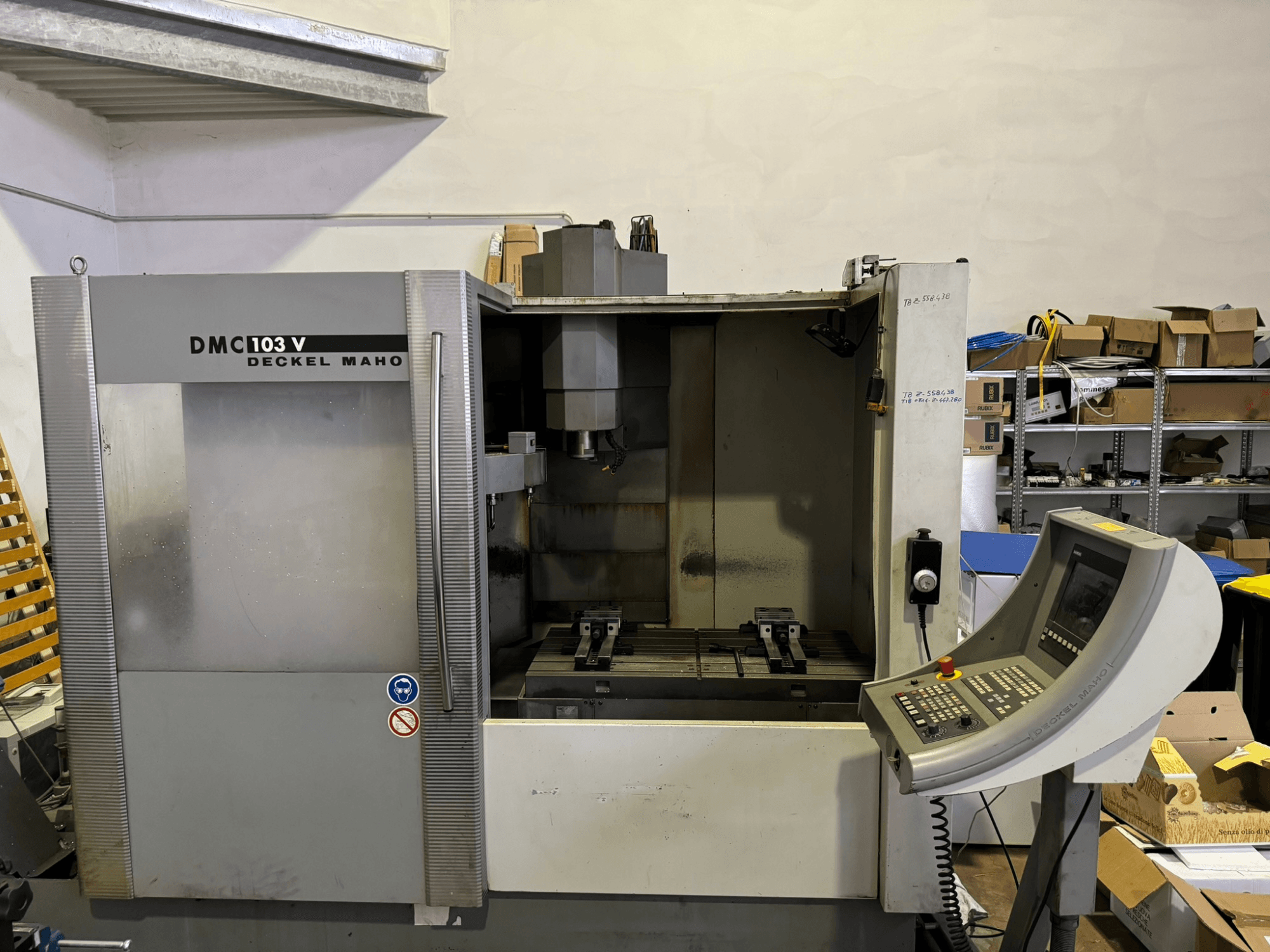 DMC 103 V Deckel Maho milling machine, front view, showing operational panel, metal parts, and storage area in background.