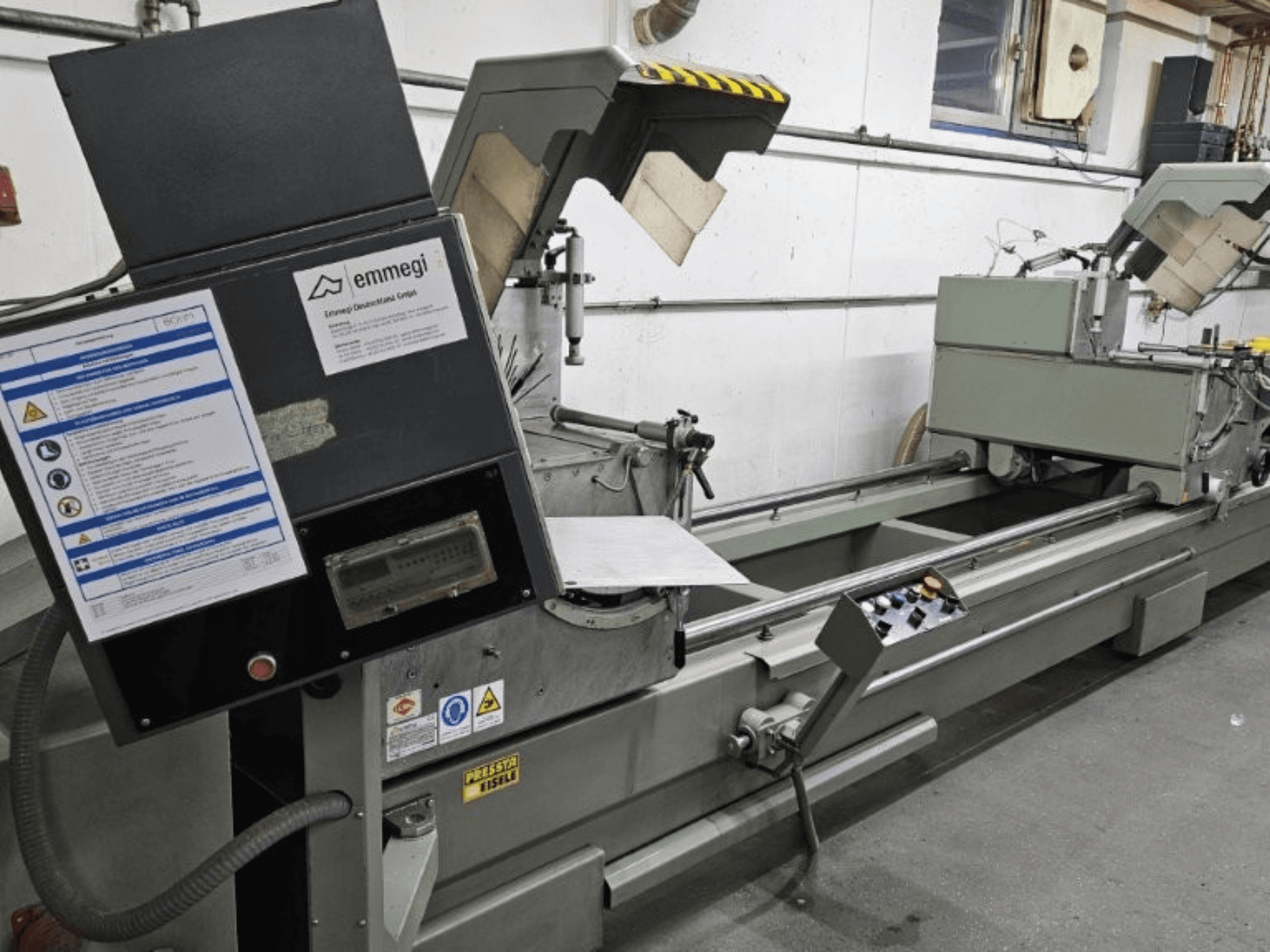 Emmegi industrial cutting machine, front view, features control panel, safety labels, and operational components.