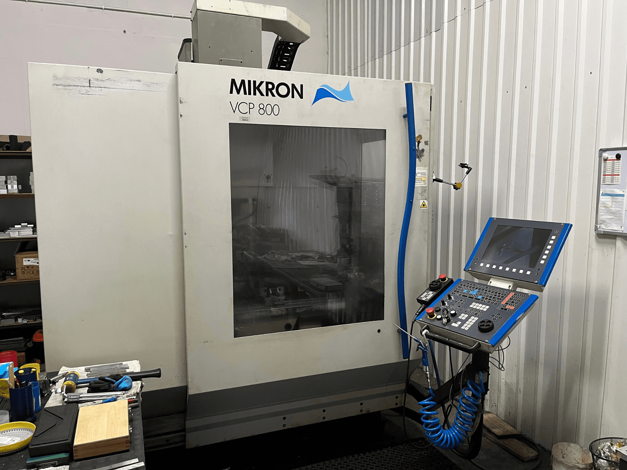 MIKRON VCP 800 vertical machining center, front view, with control panel and tools on a workbench in the foreground.