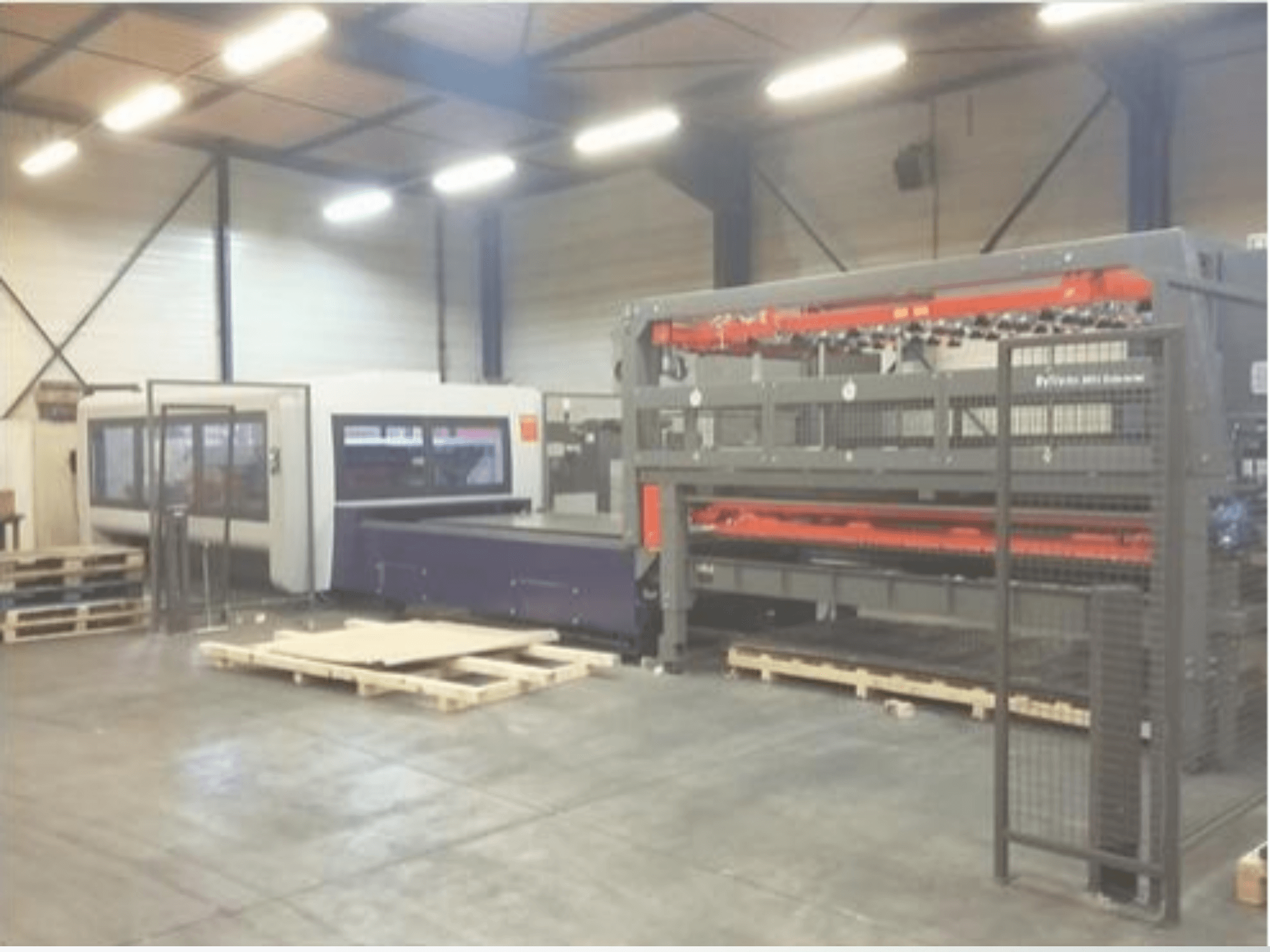 Industrial machinery setup in a warehouse; includes a gray laser cutter and a purple CNC router, front view with pallets.