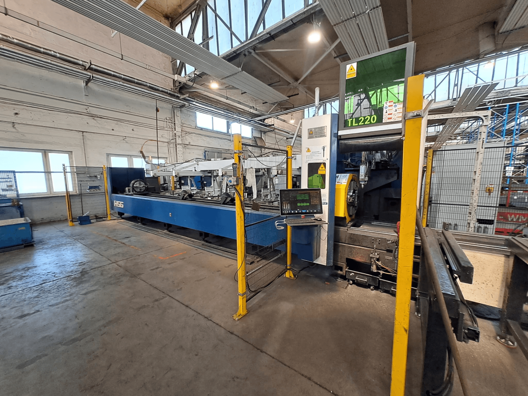 Front view of HSG HS-TL220 tube cutting machine with control panel and safety barriers in a factory setting.