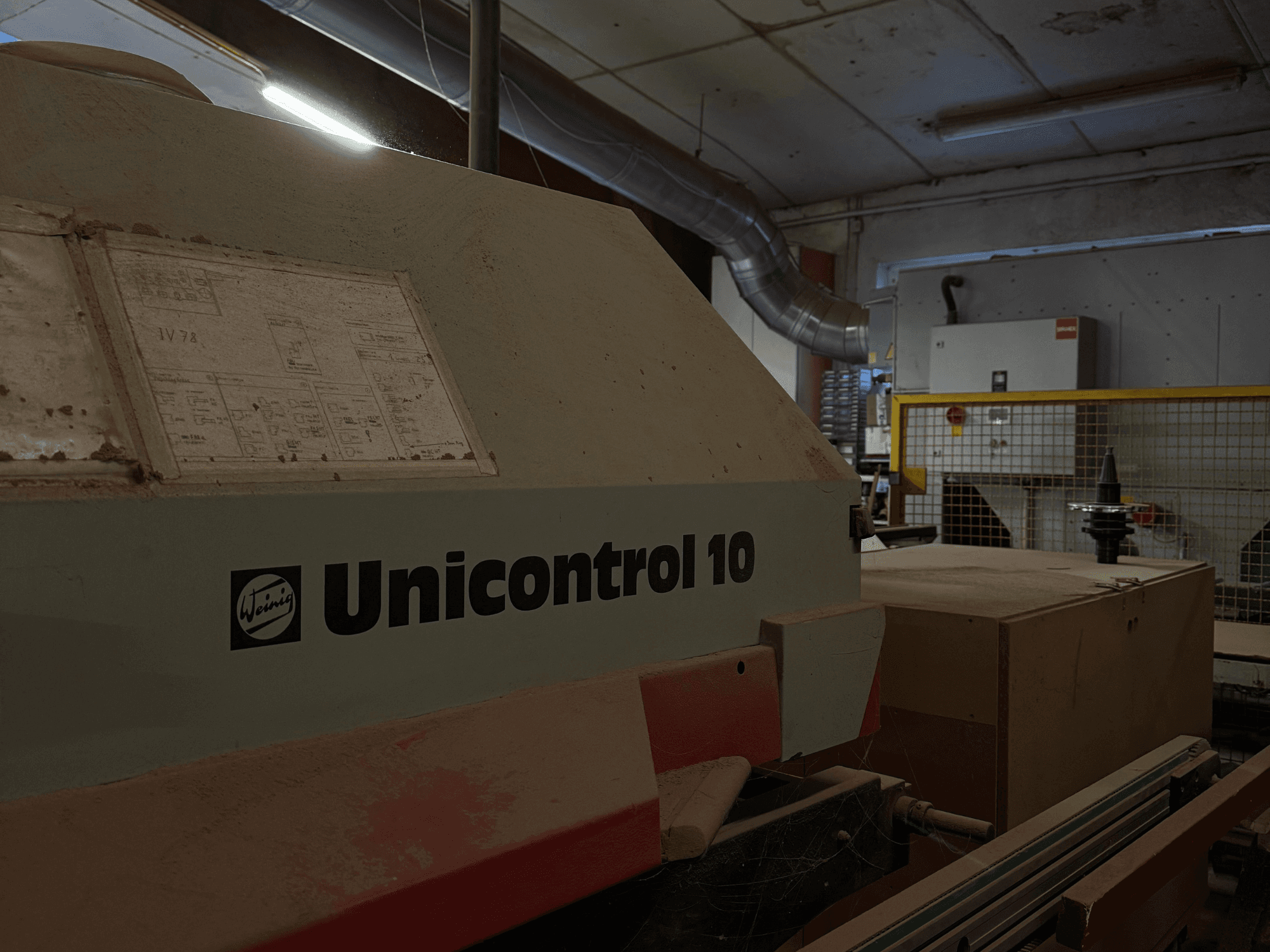 Weinig Unicontrol 10 machine viewed from a side angle, dusty surface, technical schematics visible on the front panel.