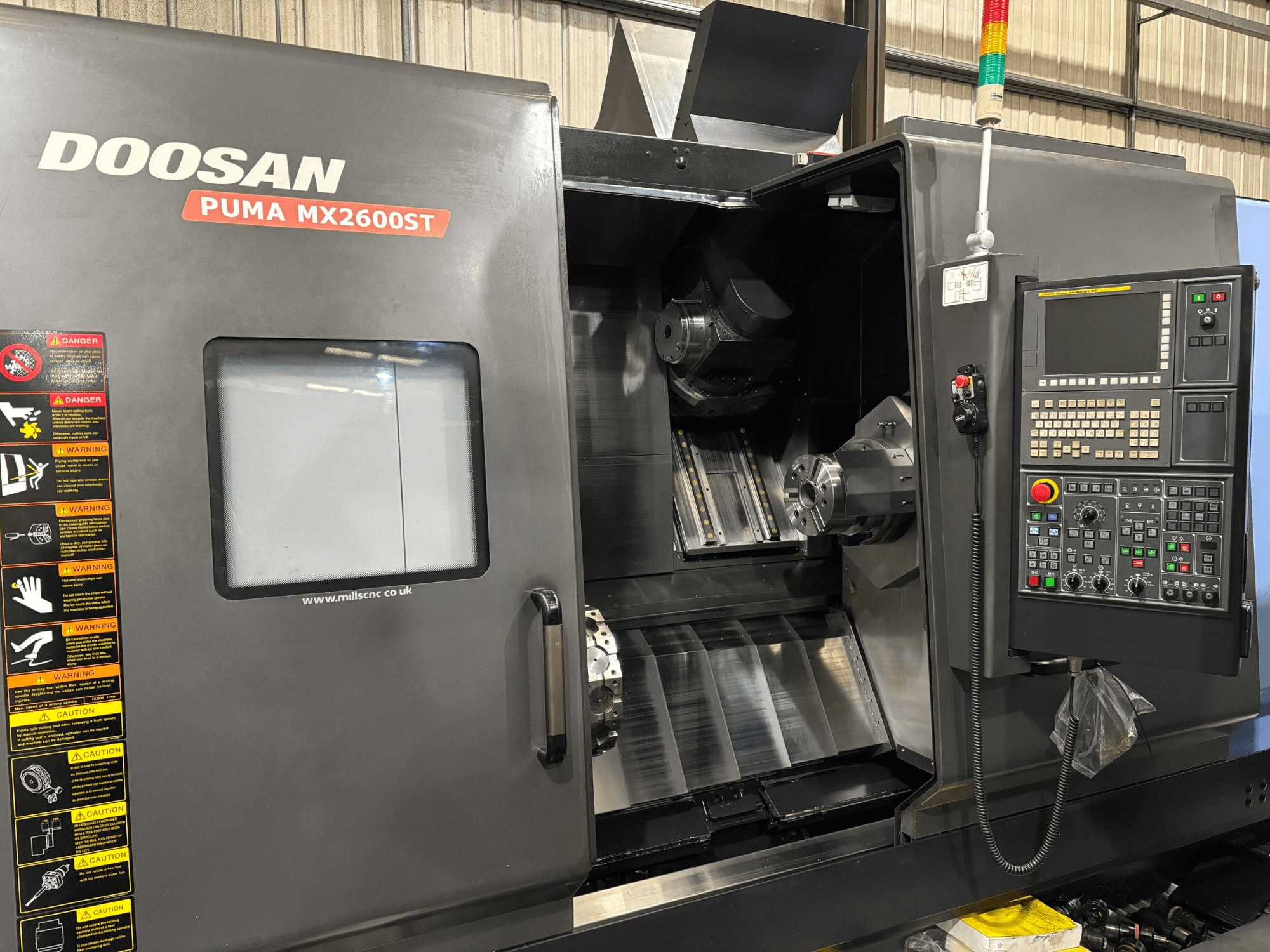 Doosan PUMA MX2600ST CNC lathe, front view, showing control panel, spindle, and machining area with visible safety warnings.