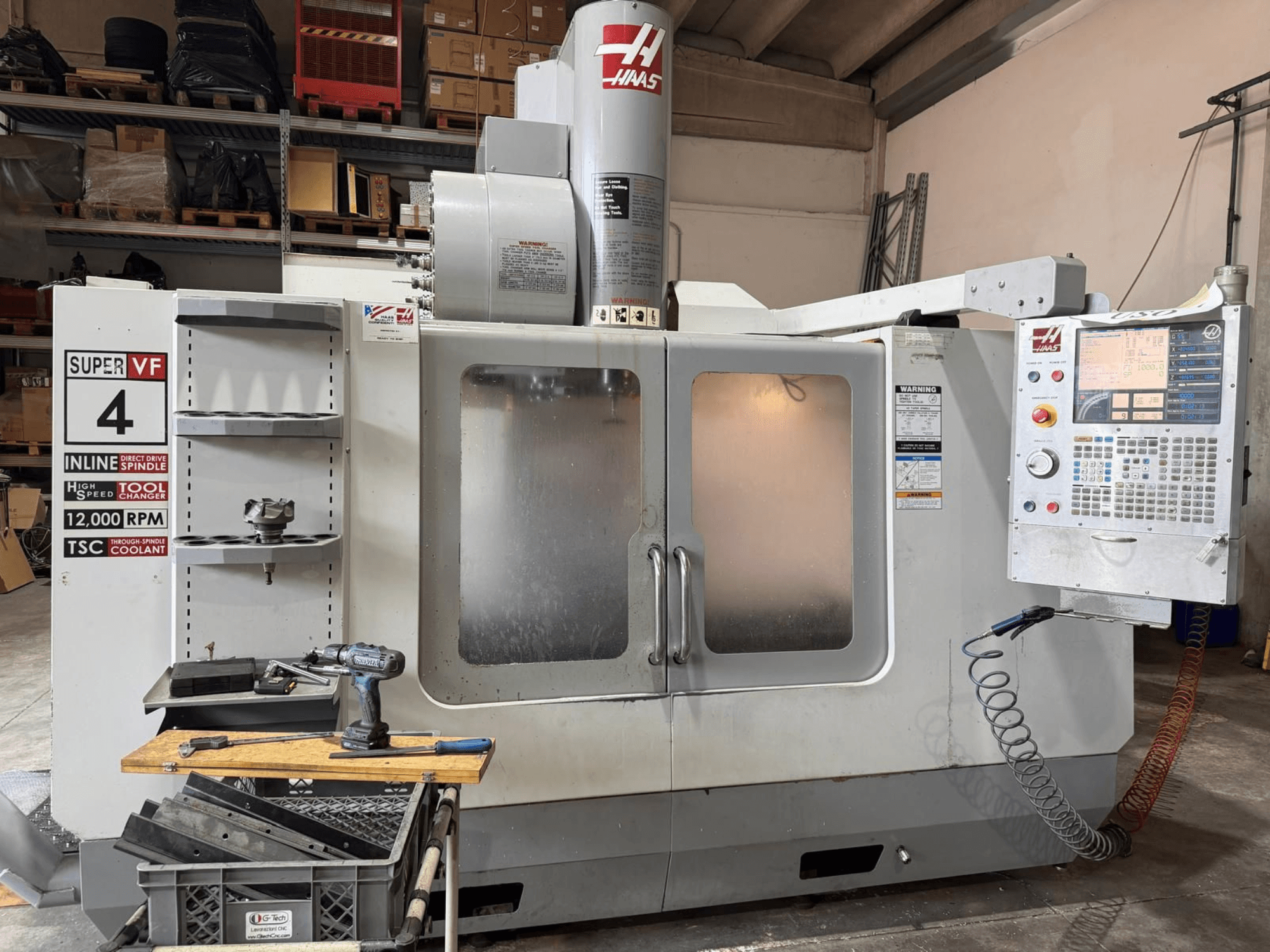 Front view of HAAS VF-4SSHE vertical machining center with controls, tool rack, and 12,000 RPM spindle; high-speed, precision machine.