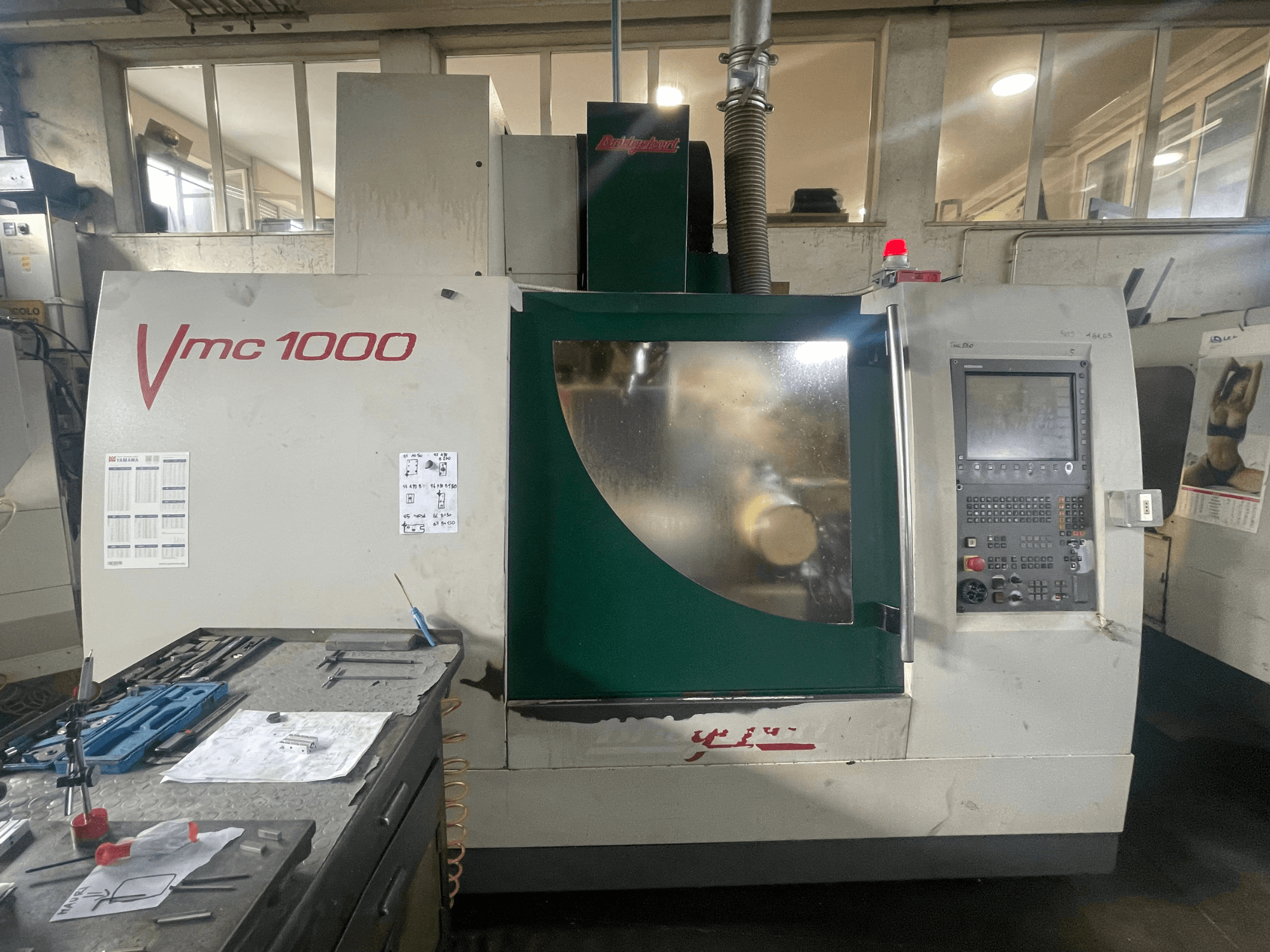 Bridgeport VMC 1000/30 vertical machining center, front view, displaying control panel and main body, with tools nearby.