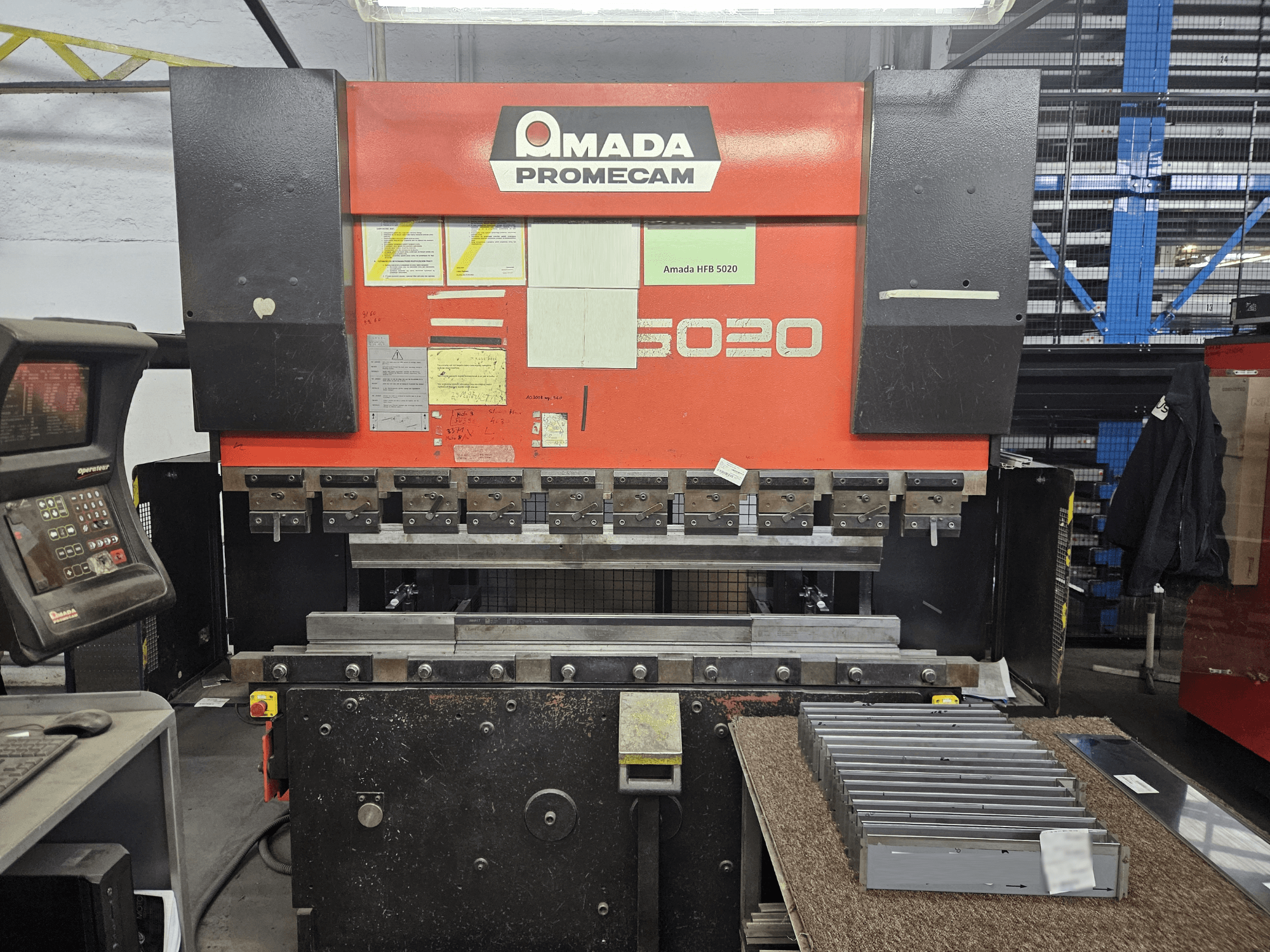 Amada HFBO 5020 press brake in front view, featuring control panel and stacked metal parts on work surface.