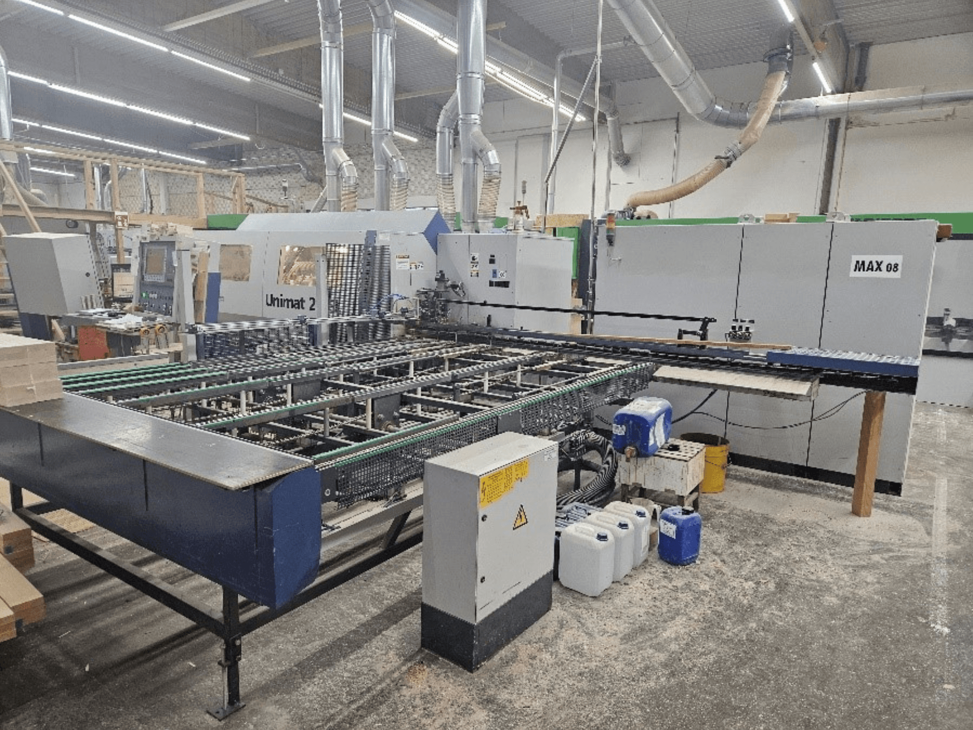 Side view of a Unimat 2 CNC machine in a workshop, featuring conveyor belts and technical components with visible Max 08 unit.