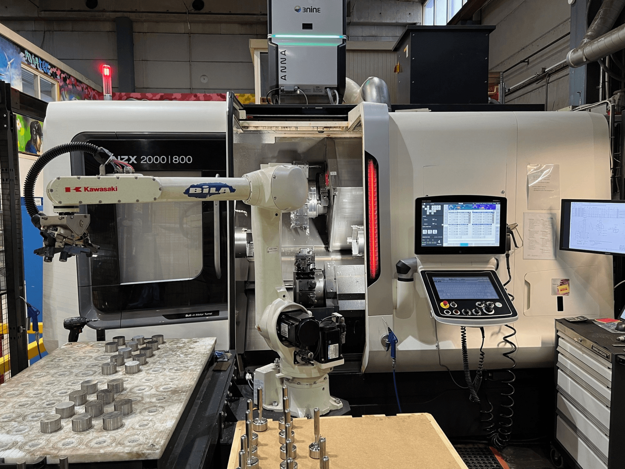 Horizontal turning machine DMG MORI NZX 2000/800SY in a workshop, with Kawasaki robotic arm and controls visible.