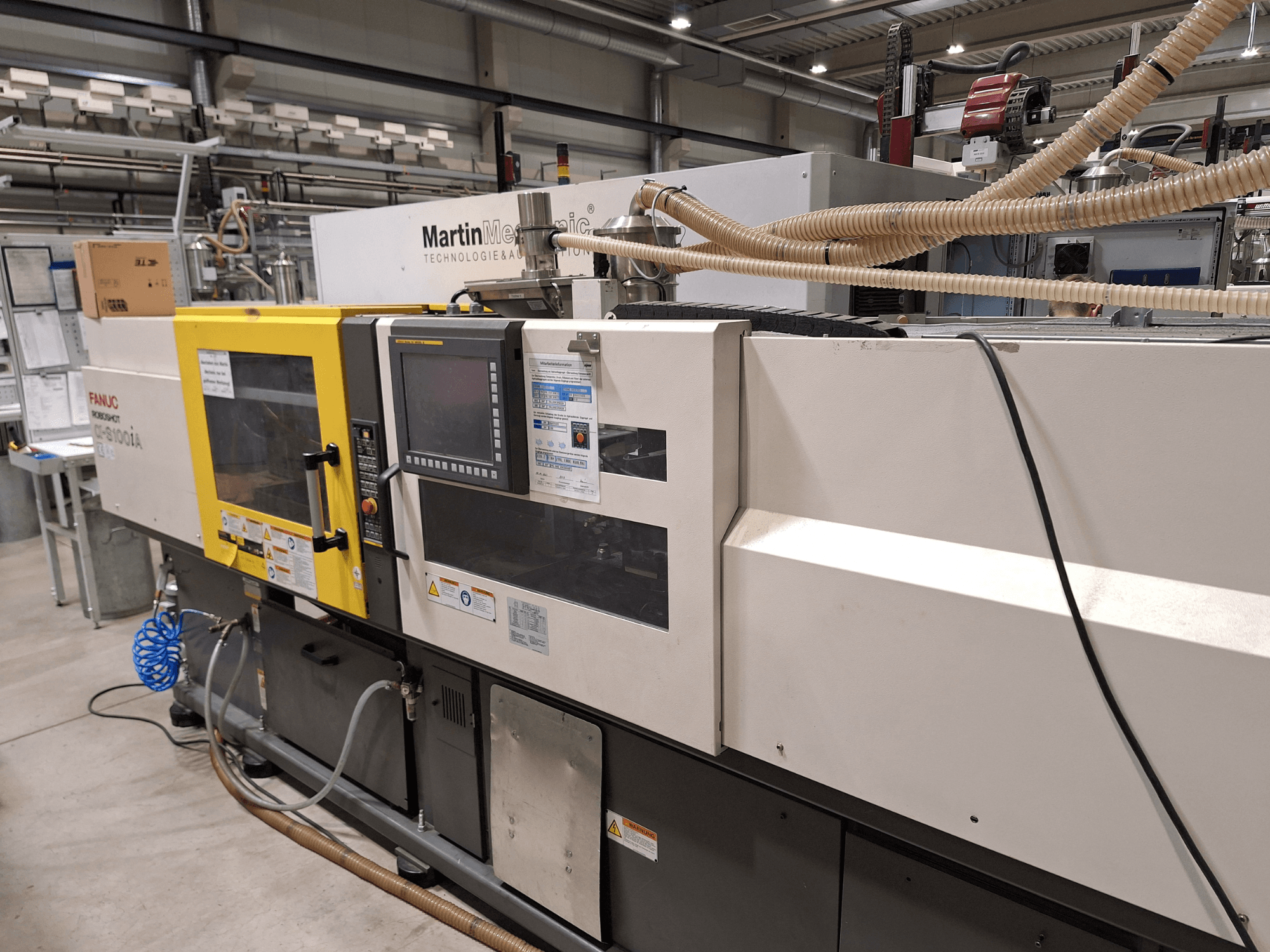 FANUC Roboshot S100iA electrical injection moulding machine, side view, equipped with touchscreen and safety labels.