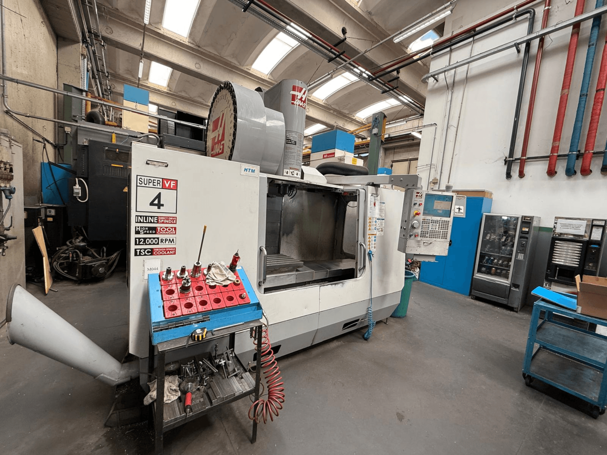 HAAS Super VF 4 CNC milling machine with a control panel, 12,000 RPM spindle, and tools on a blue storage rack, side view.