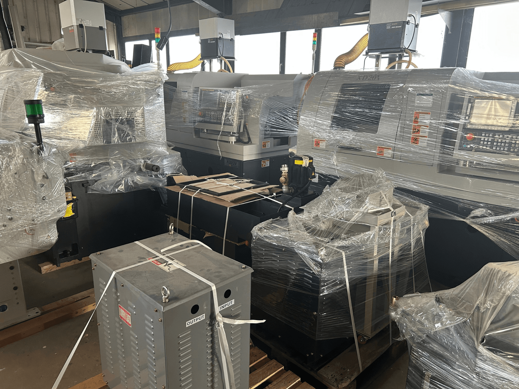 Hanwha XD20 Swiss Type Turning Machine, front view, plastic wrapped, showing control panel and attachments in a warehouse setting.