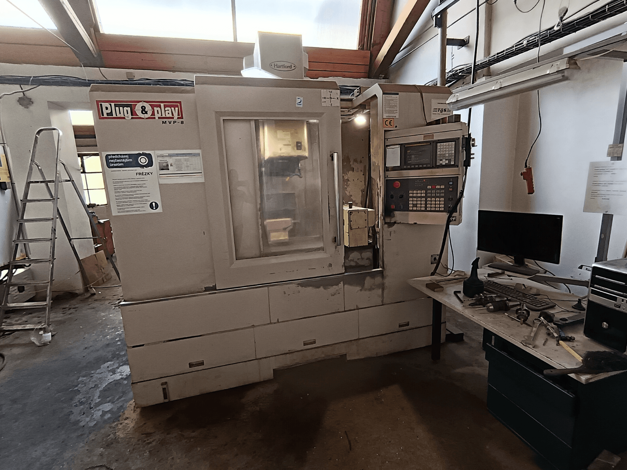 Vertical machining center HARTFORD MVP-8A viewed from the front, featuring a control panel and tools on the adjacent table.