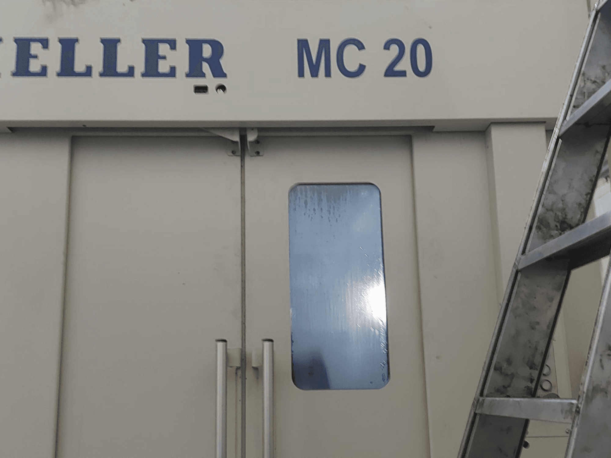 Front view of HELLER MC 20 horizontal machining center, showing door handles and a small window. Ladder on the side.