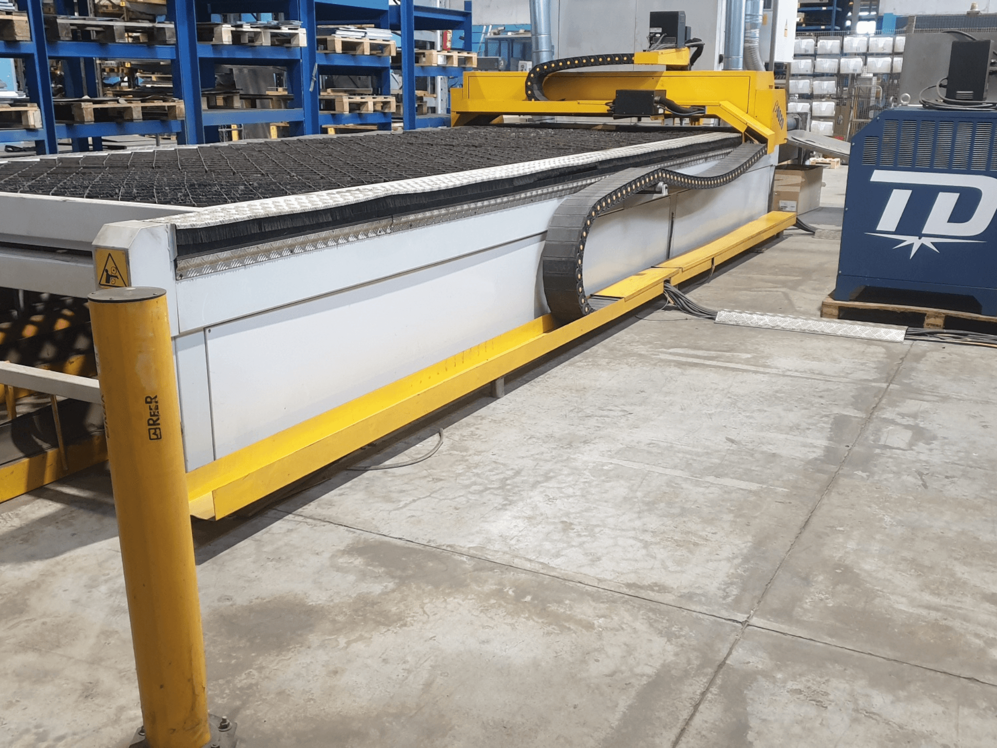 Industrial cutting machine with yellow trim, front view, featuring a textured bed and control panel, placed on a factory floor.