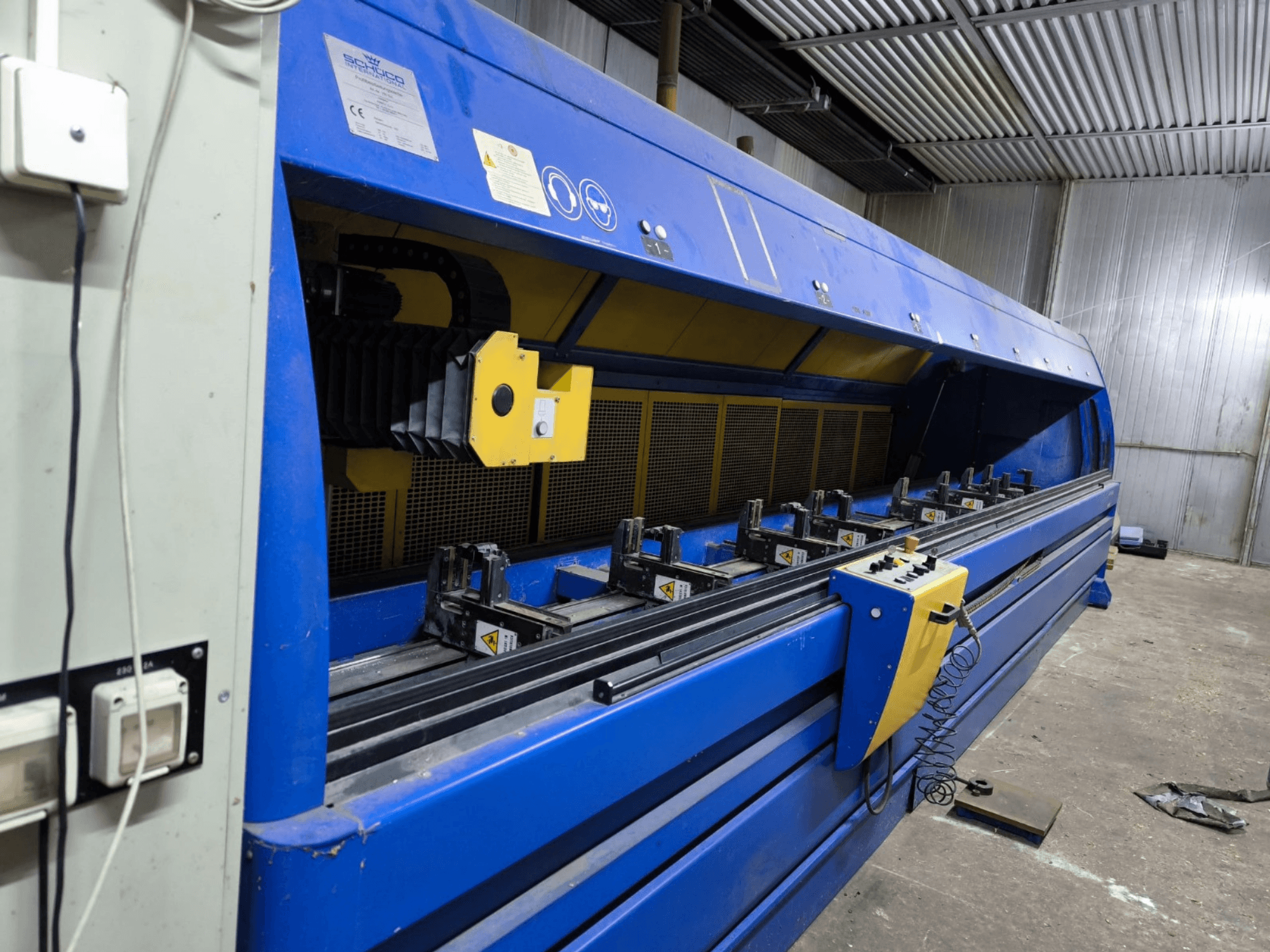 Schneider industrial cutting machine in blue, side view, with control panel, belts, and multiple clamping stations visible.