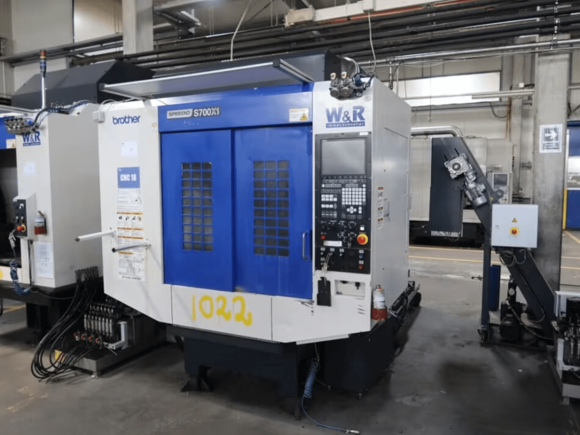 Brother Speedio S700 X1 vertical machining center, front view, featuring control panel and blue doors, in an industrial setting.