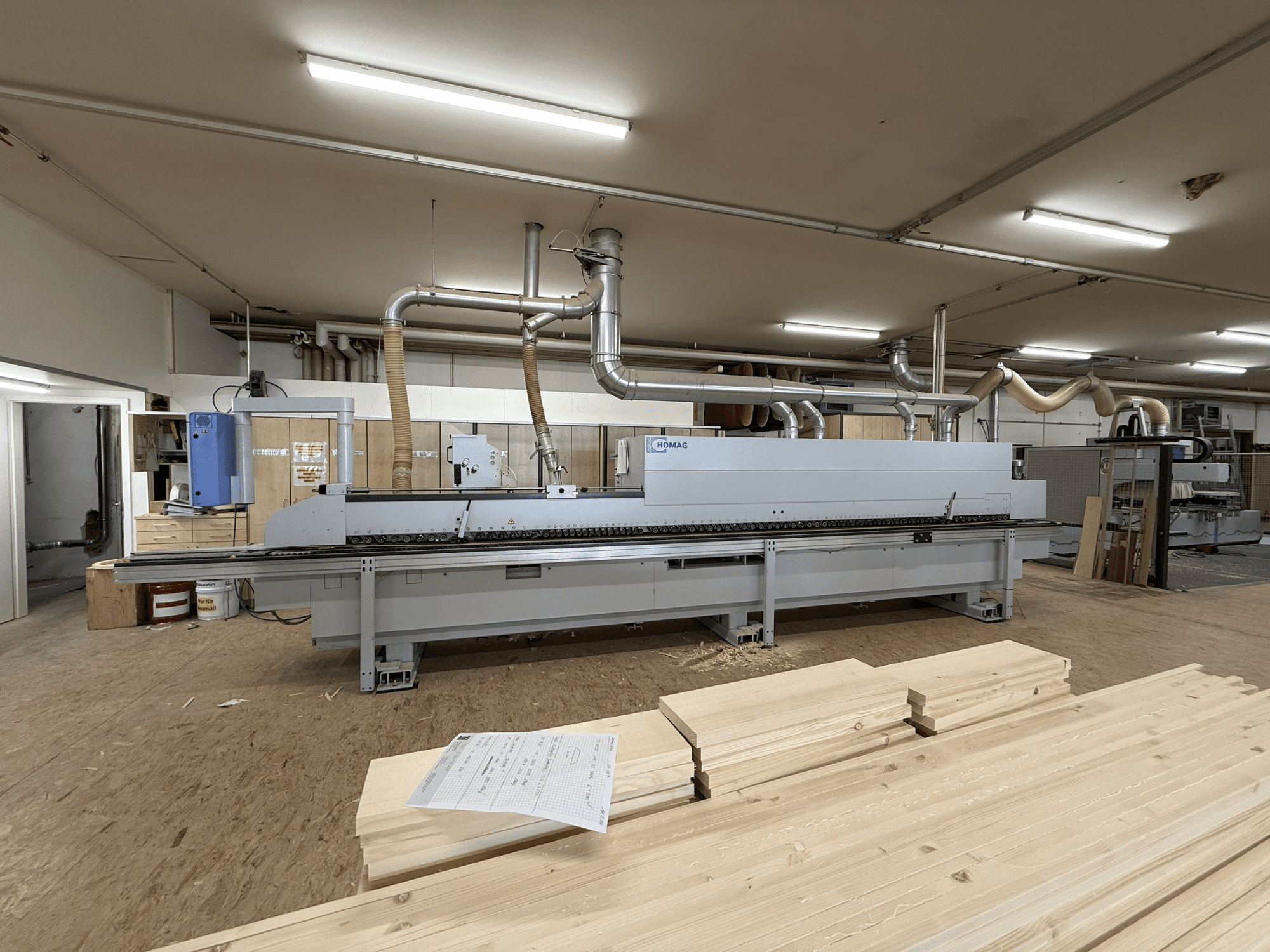HOMAG KAL211 Edgebander in a workshop, front view, with wood boards and machinery in a well-lit environment.