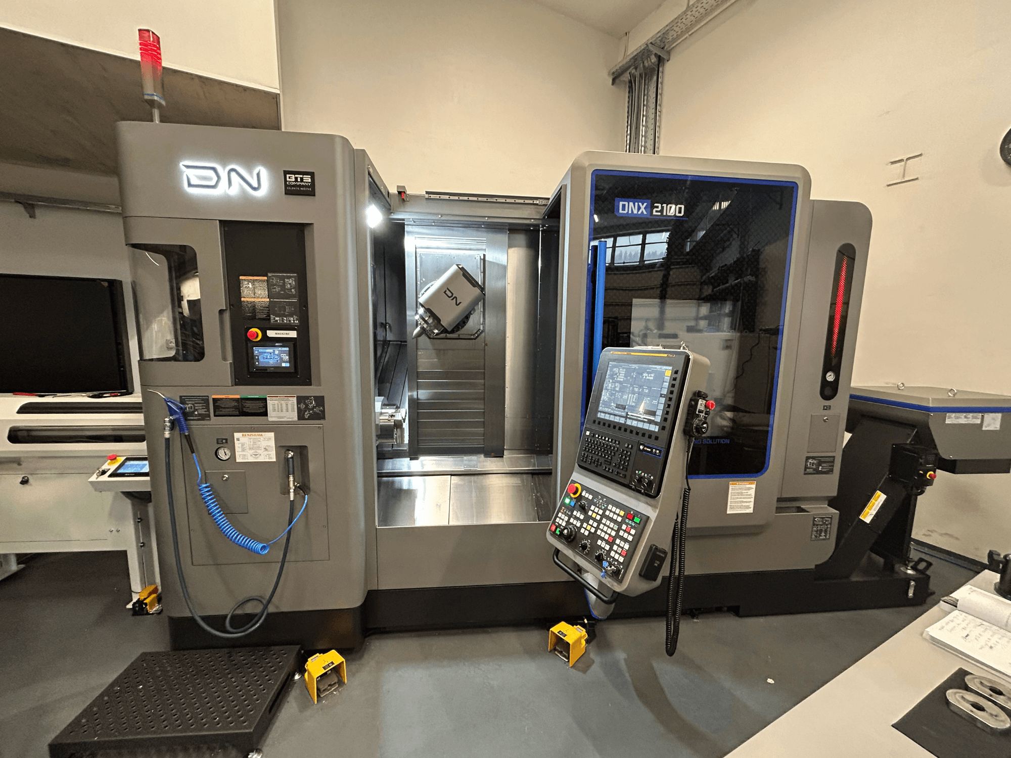 DN ONX 2100 CNC machine, front view, features control panel, work area, and tool. Equipped with safety light and operation indicators.