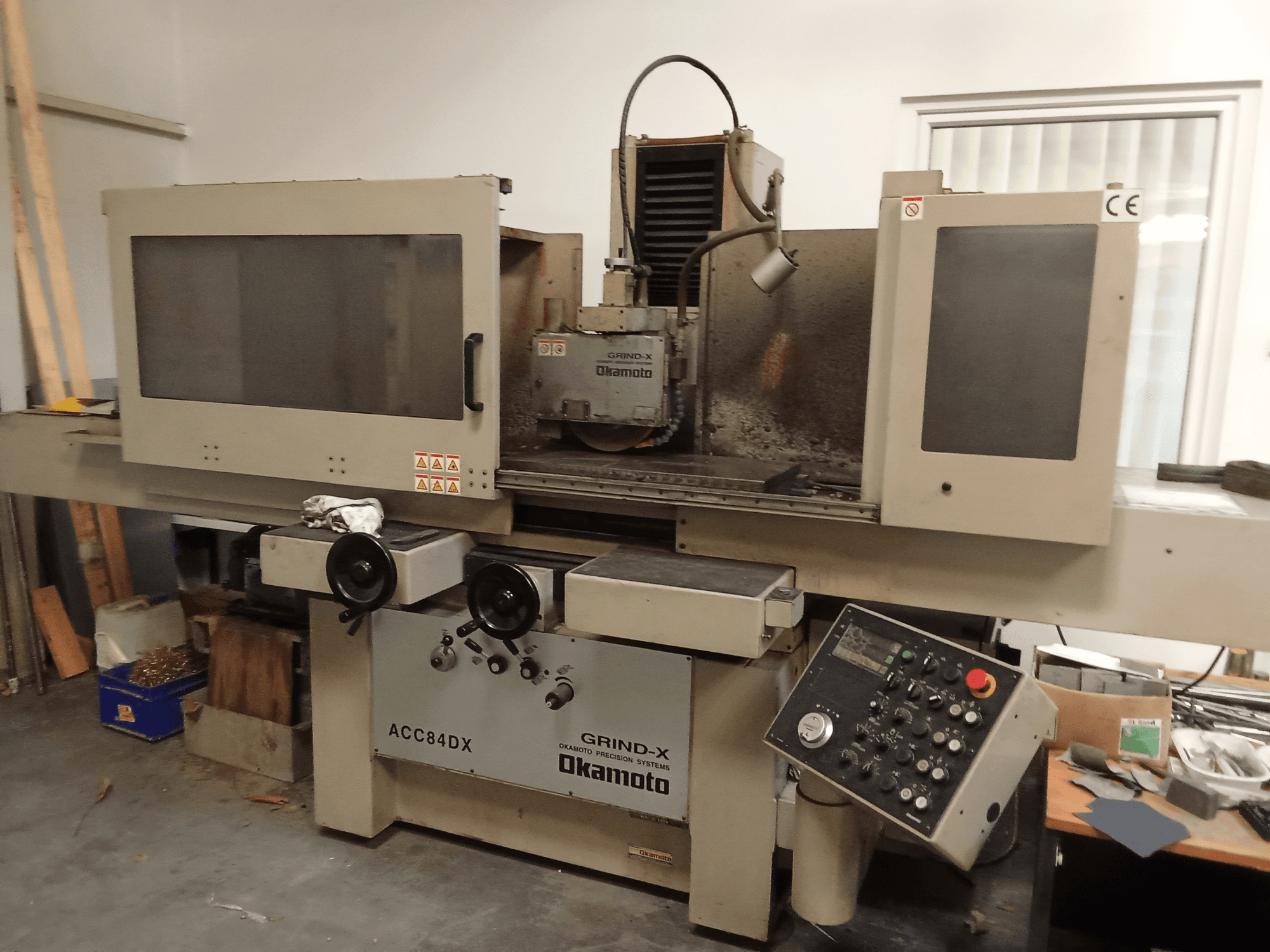 Front view of OKAMOTO ACC84 DX surface grinding machine, featuring control panel and grinding wheel enclosure.