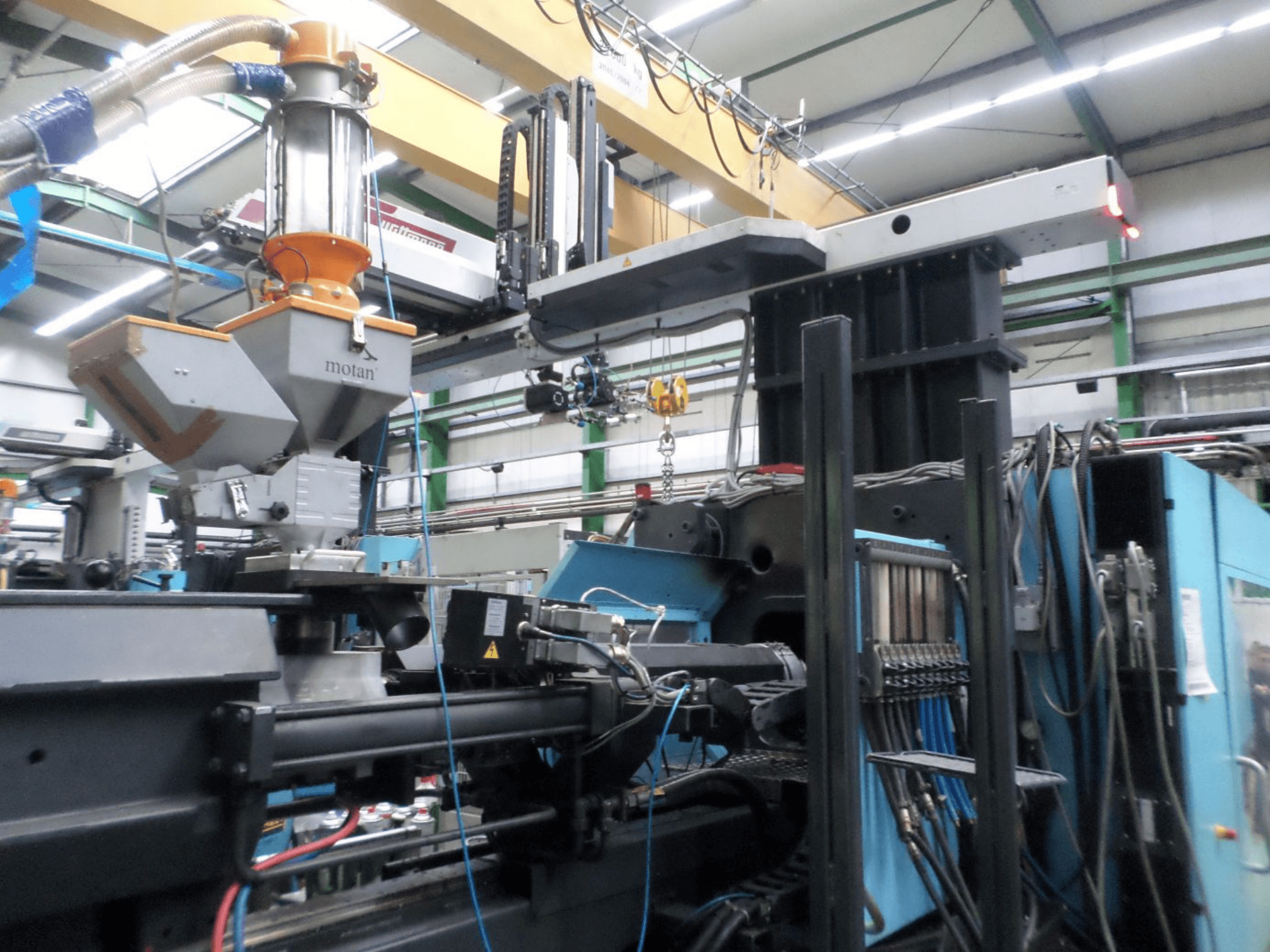Hydraulic injection moulding machine DEMAG D 1300, side view, showing hopper, control unit, and connections in a factory setting.