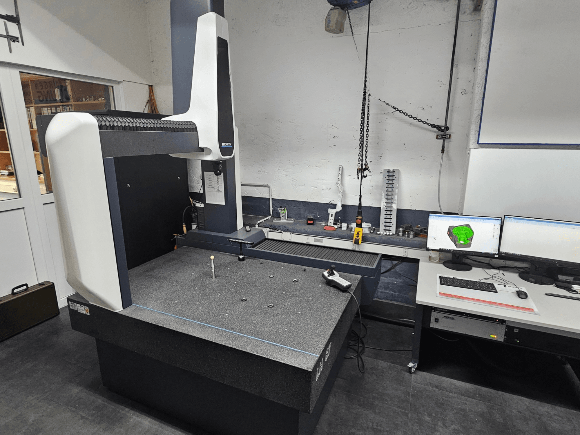 Coordinate Measuring Machine Wenzel LH 87 in a workshop, front view, with a probe on the granite table and dual monitors displaying CAD design.