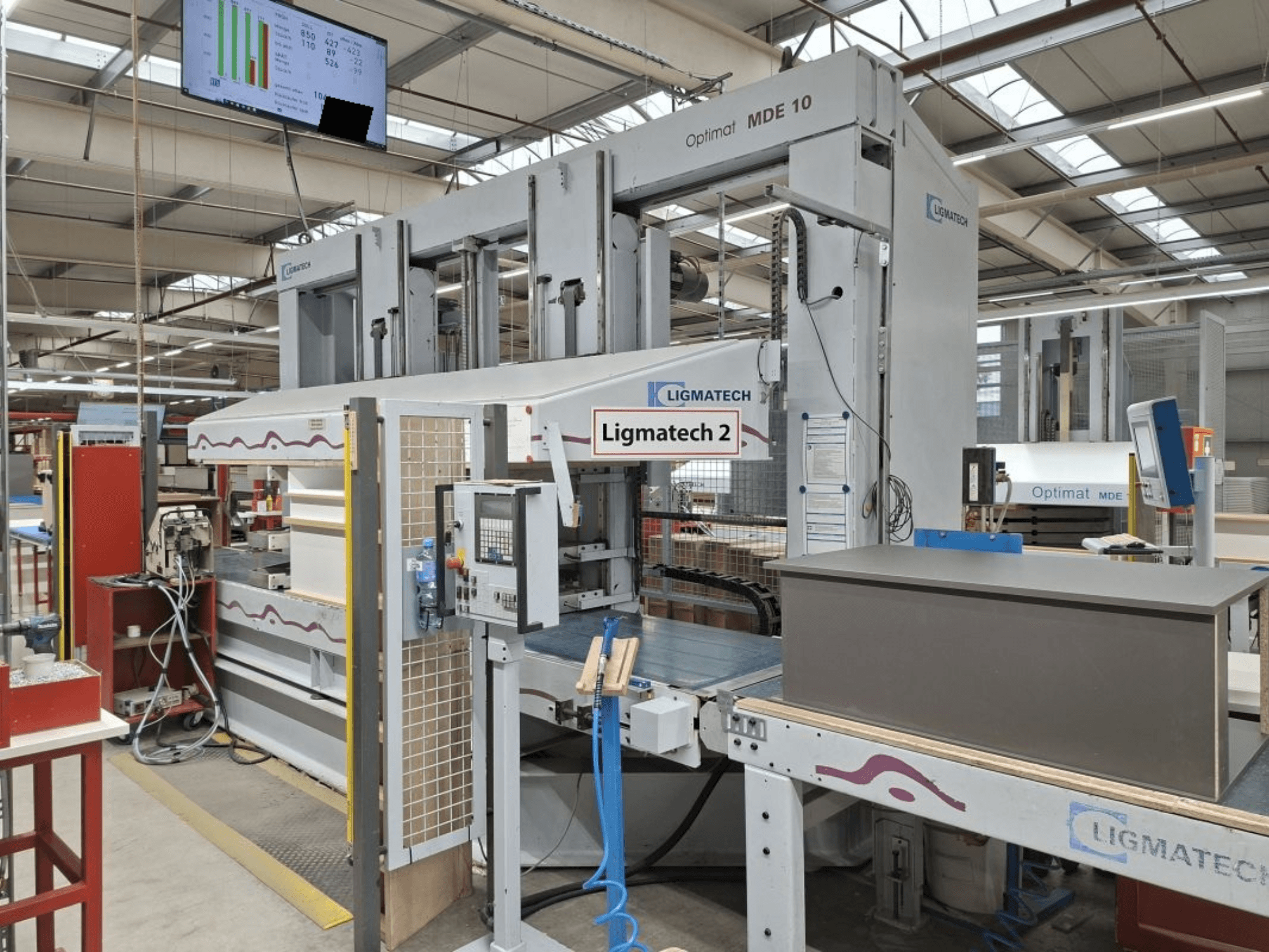 LIGMATECH Optimat MDE 10 machine in a workshop, side view showing controls and wood piece on conveyor.