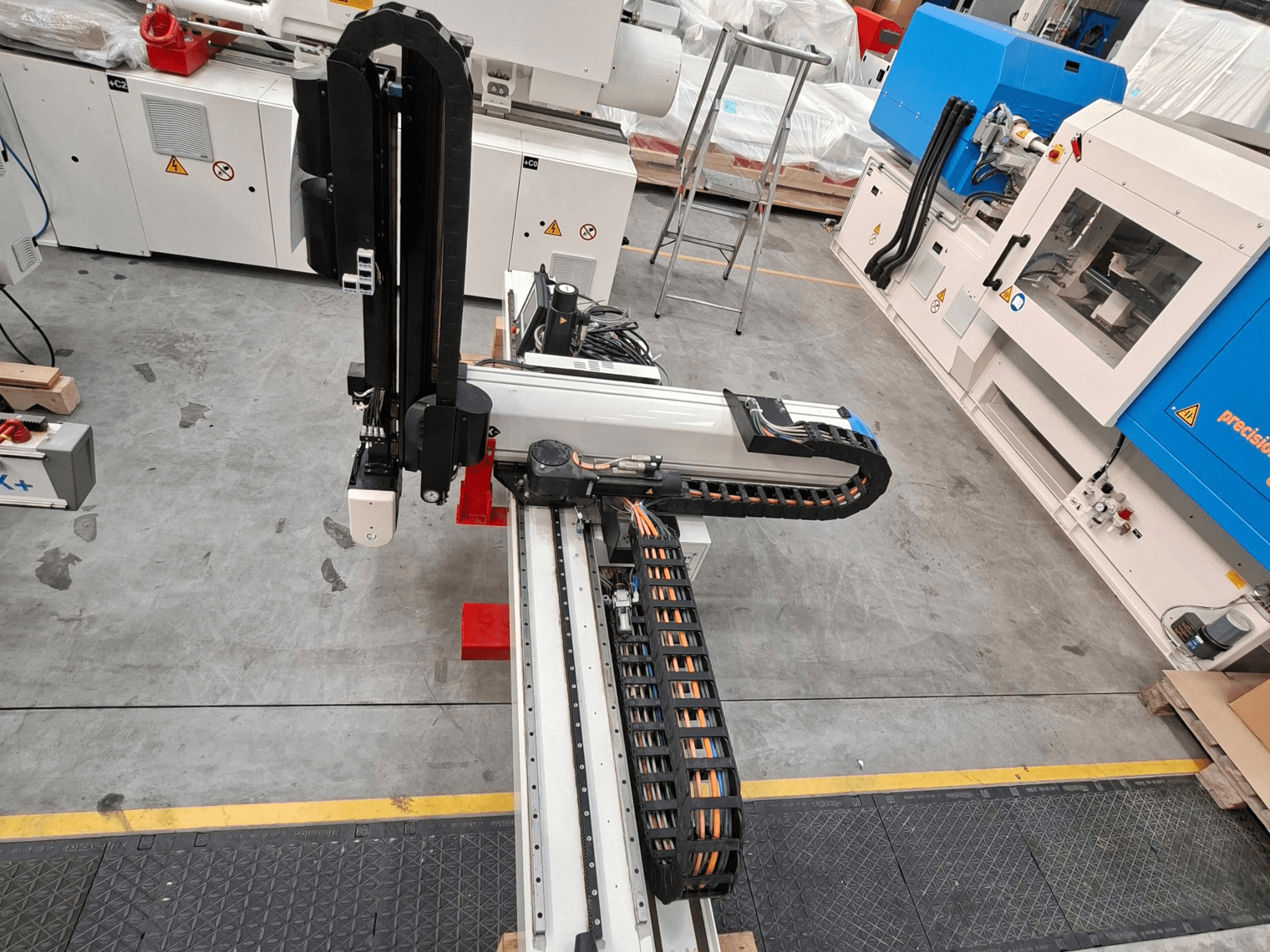 Plastic processing machine Krauss Maffei LRX150-MC5 in overhead view, showcasing robotic arm and cable track on factory floor.