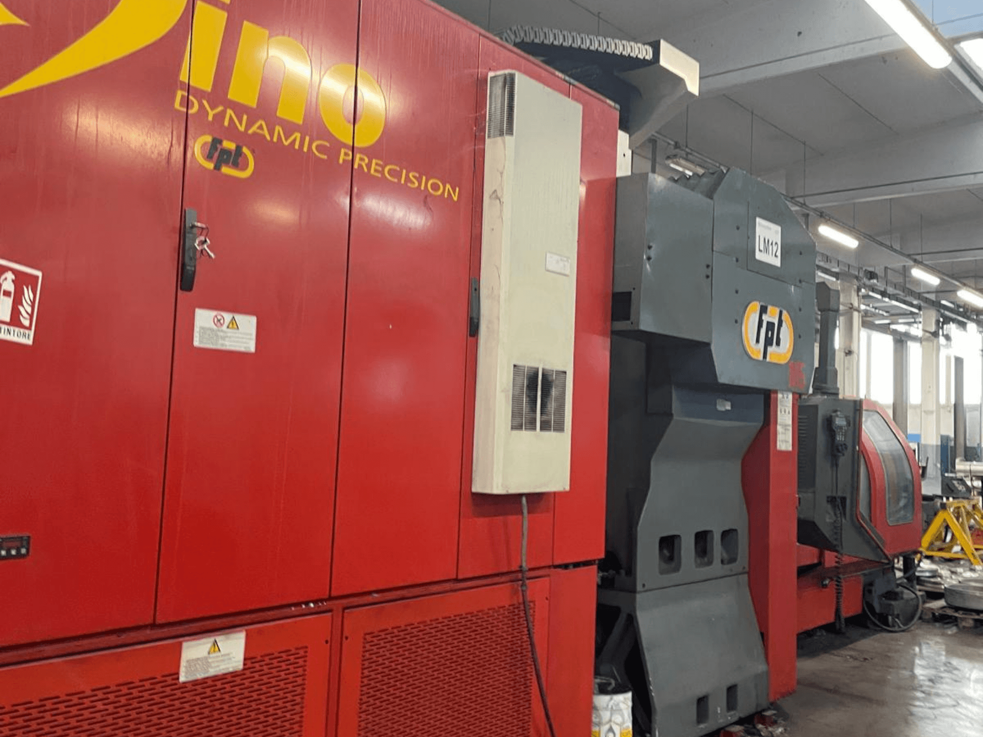 FPT DINO vertical machining centre in red, side view showing control panel and machining area in an industrial setting.