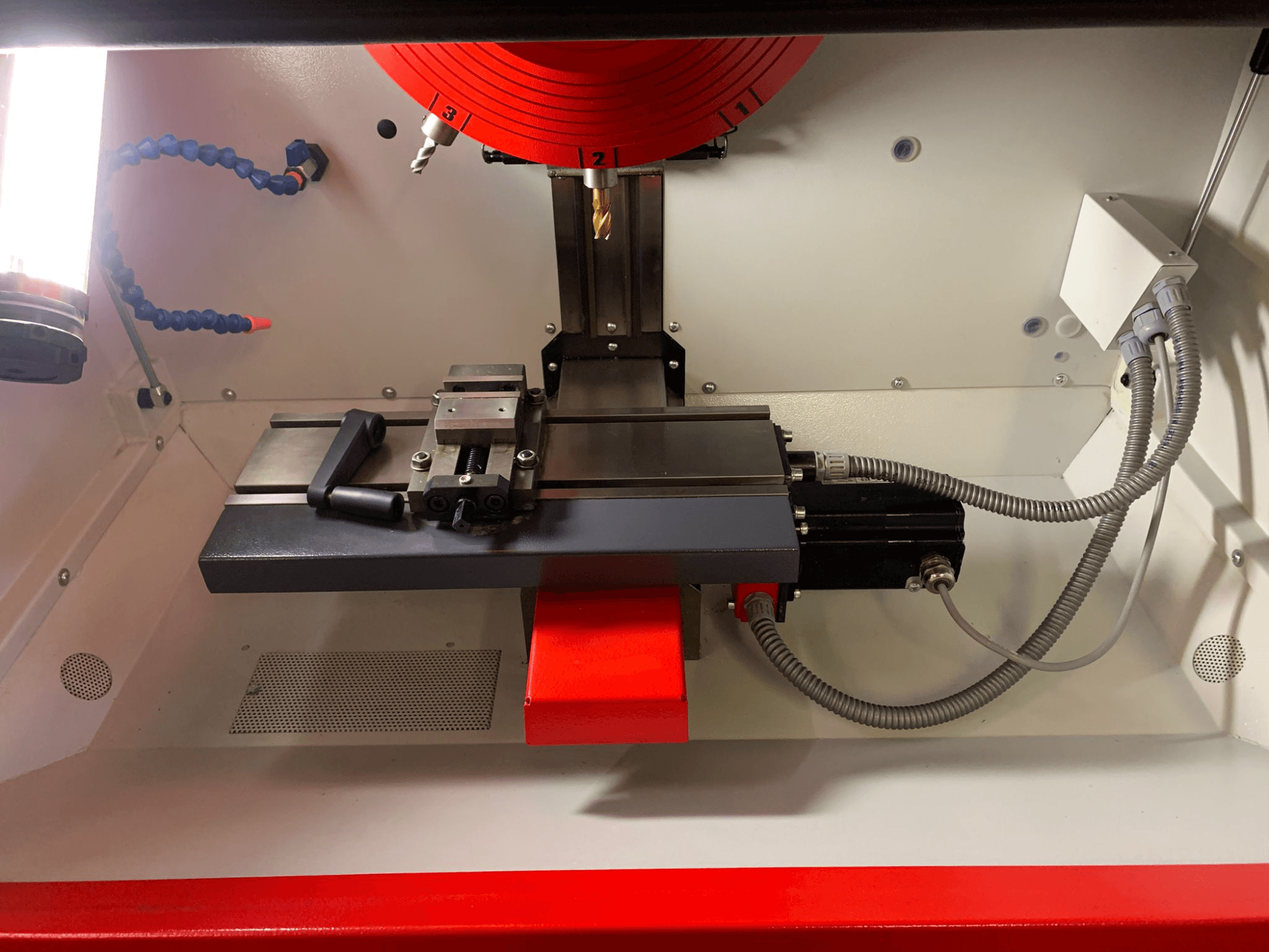 Inside a machining tool, featuring a linear guide, spindle, and wiring. Front view shows components and red accents.