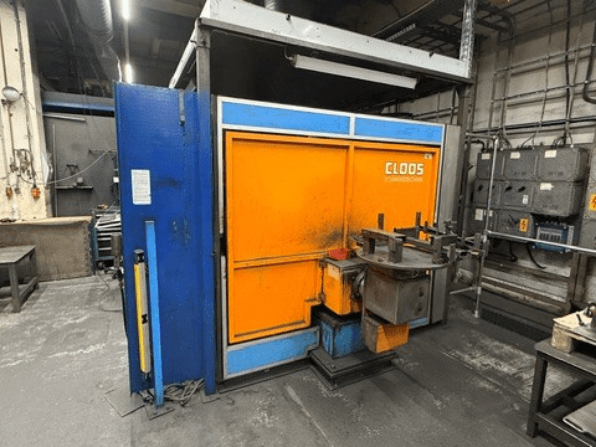 CLOOS Romat 320 welding robot in a workshop, front view showing orange and blue enclosure with control panel and tools.